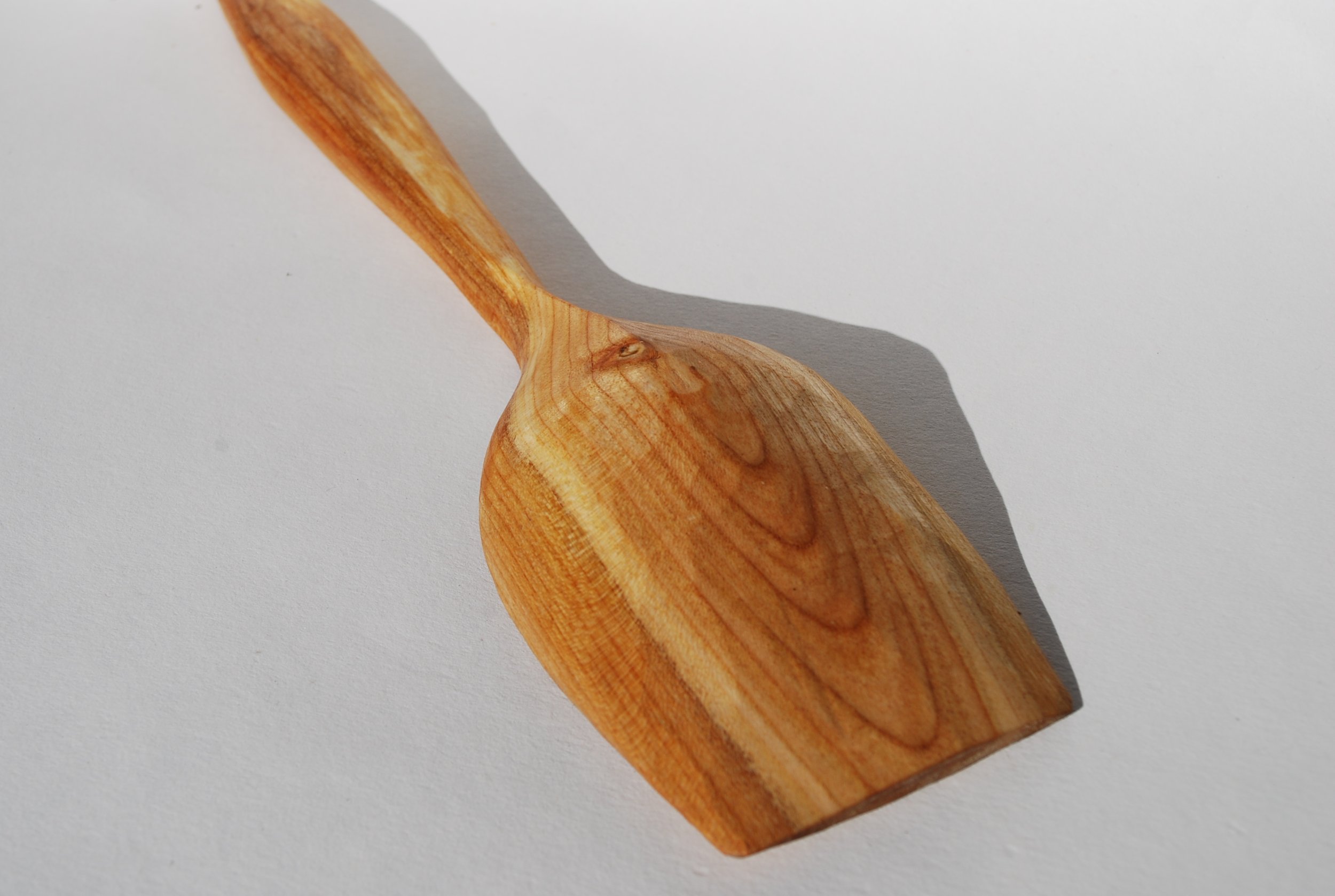 A wooden spatula with a rounded head casting a shadow on a white surface.