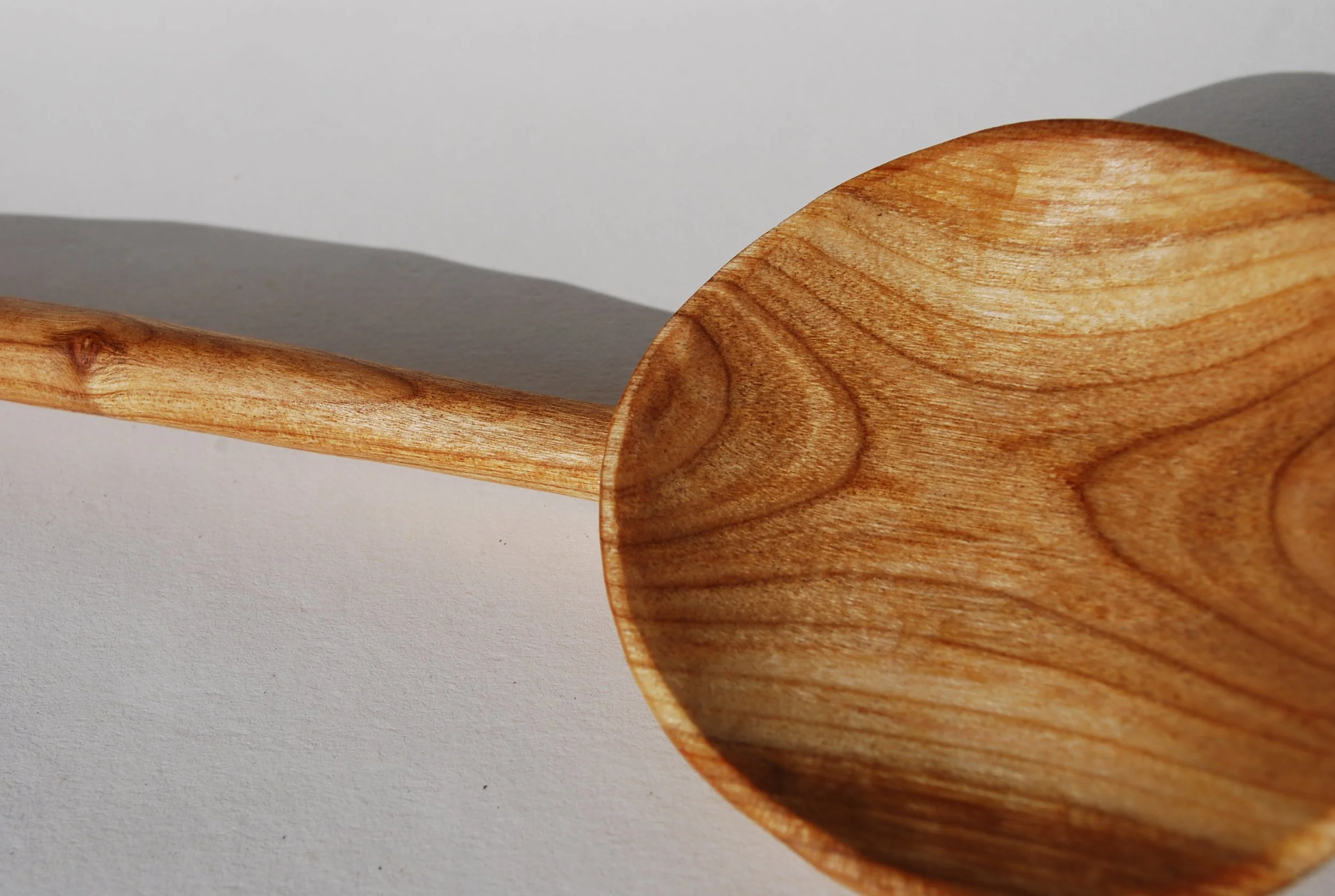 Close-up of a wooden spoon casting a shadow on a white surface.