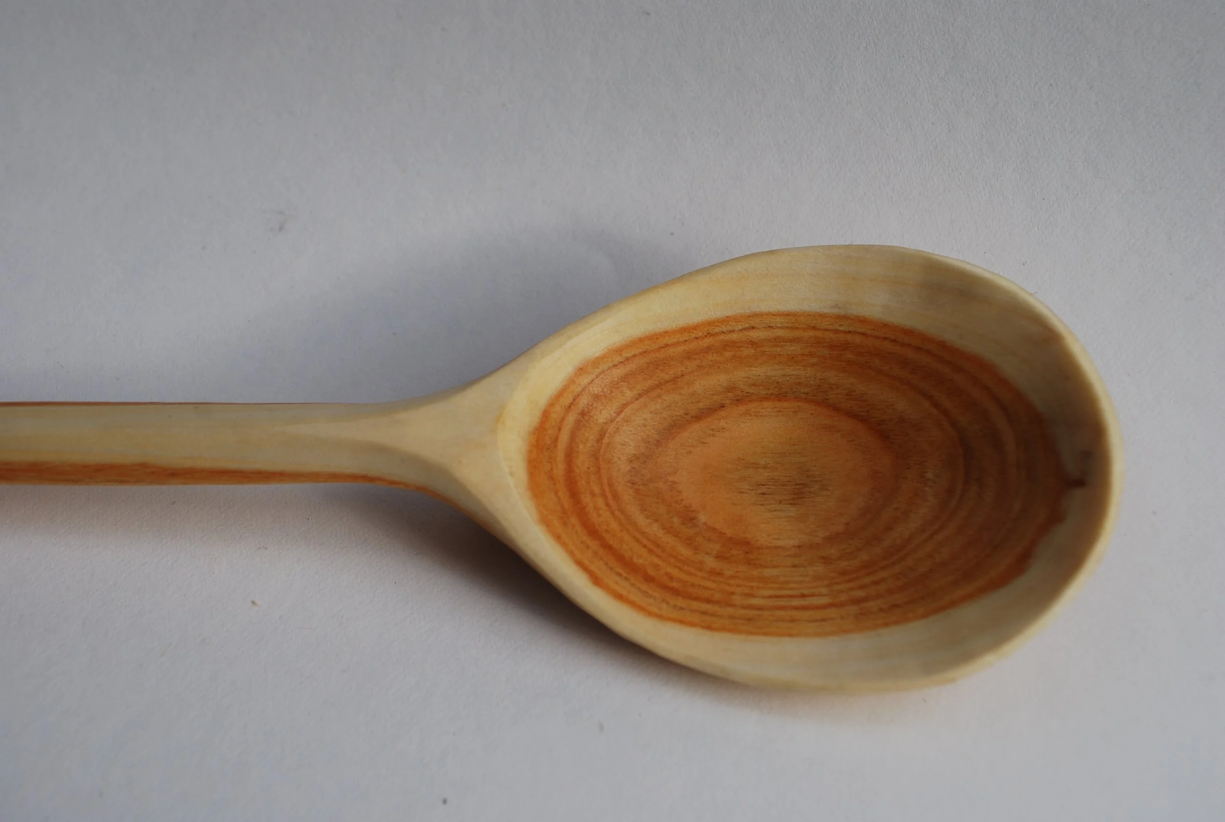 A wooden spoon with a rounded bowl and a light-colored handle, placed on a plain white surface.