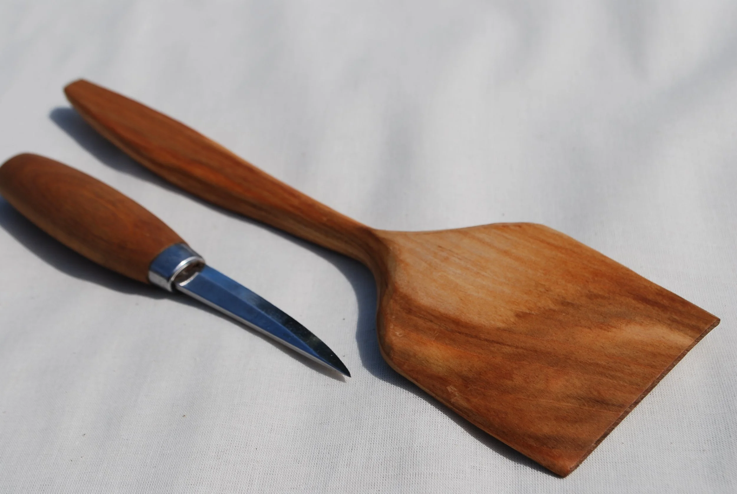 A wooden spatula and a wooden-handled paring knife placed on a white surface.