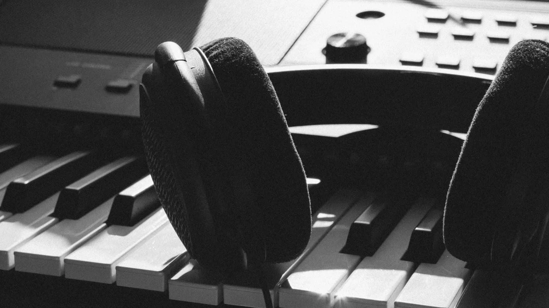 Black and white photo of headphones resting on a keyboard piano.
