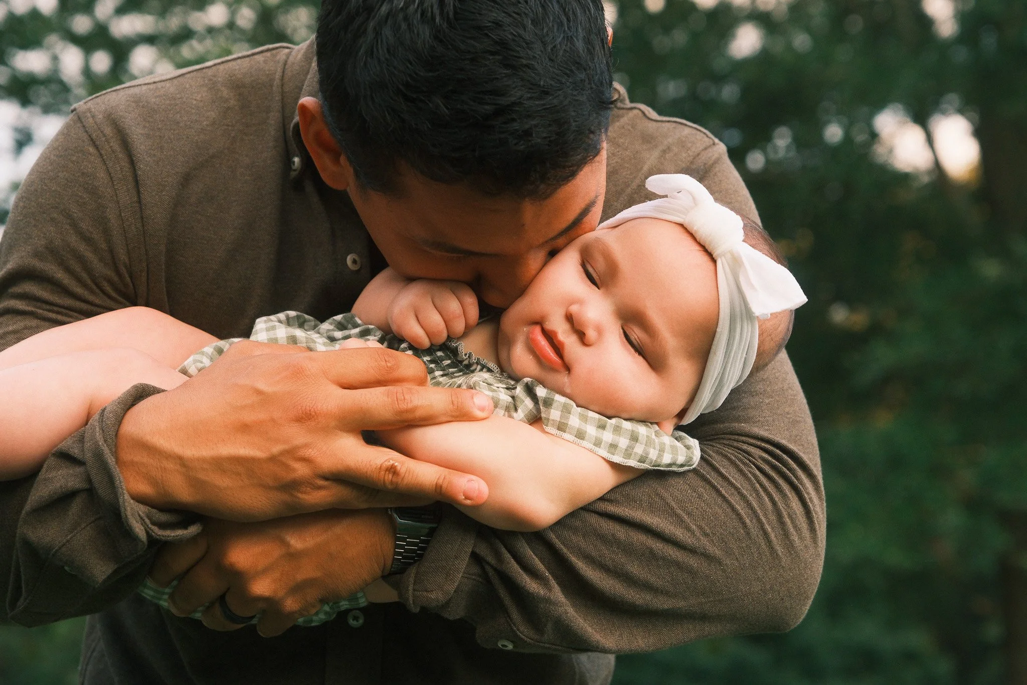 Man holding and kissing a young girl outdoors during the daytime.