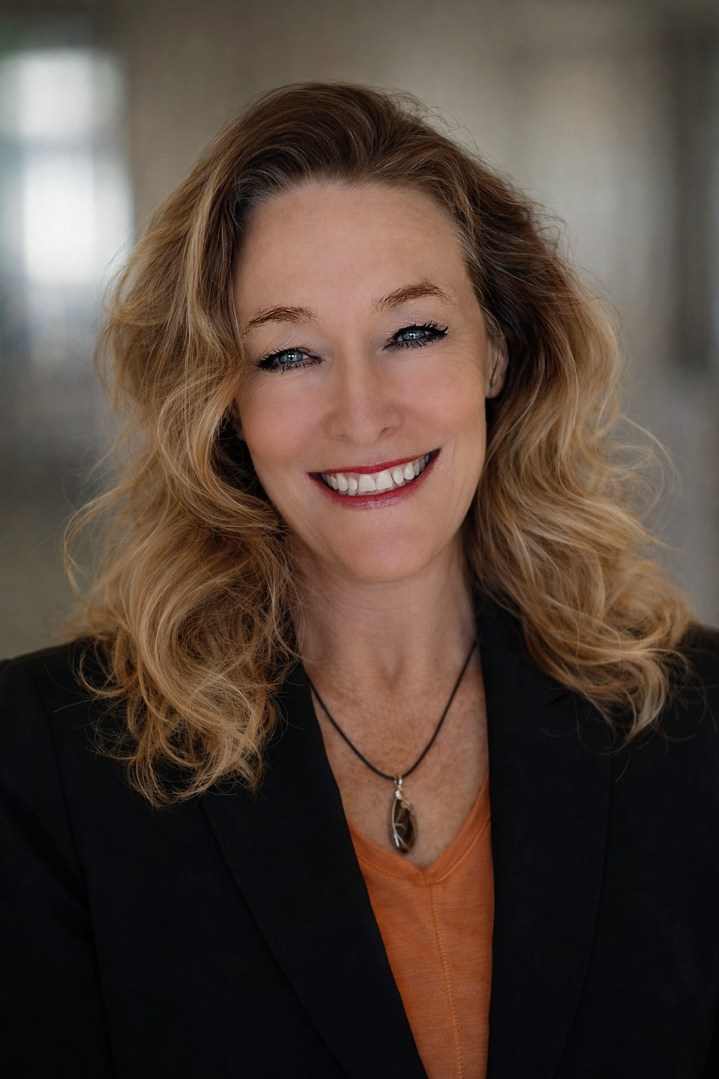 A smiling woman with blonde hair, wearing a white collared shirt and a black blazer, looking at the camera.