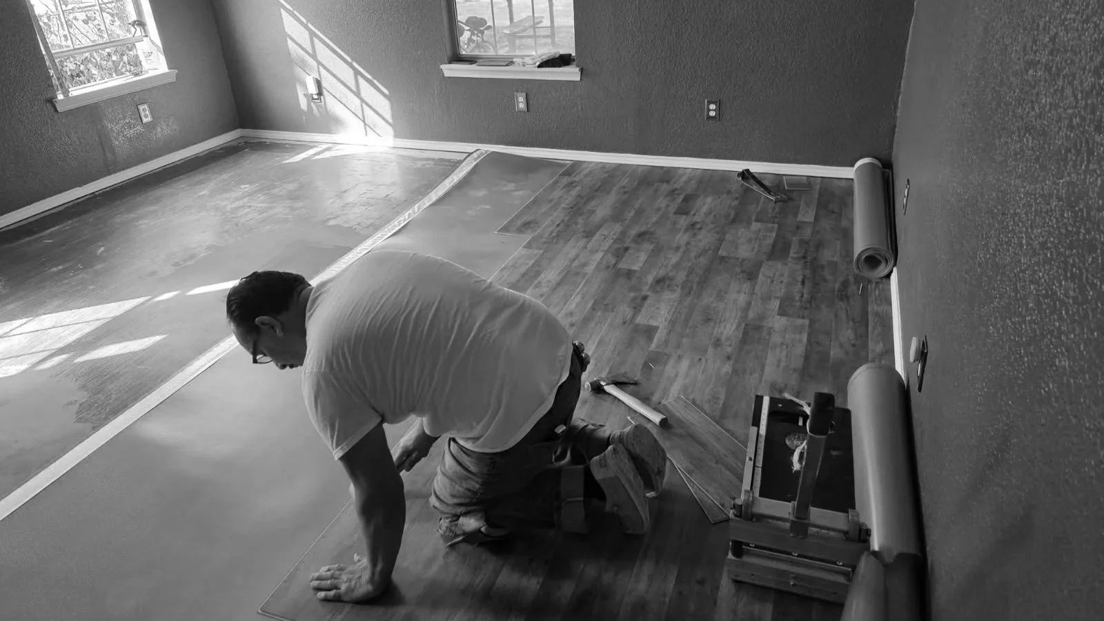 A person installing wooden flooring in a room with a window, tools, and flooring materials around.