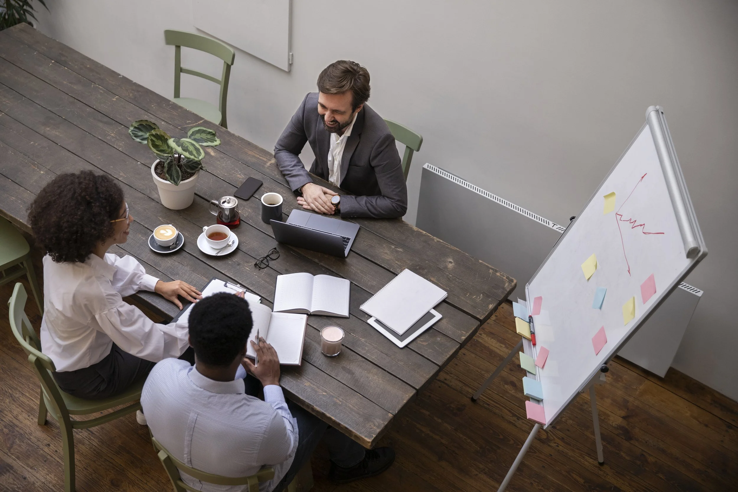 Trois personnes en réunion dans une salle de conférence, autour d'une grande table en bois, avec un tableau blanc à côté.