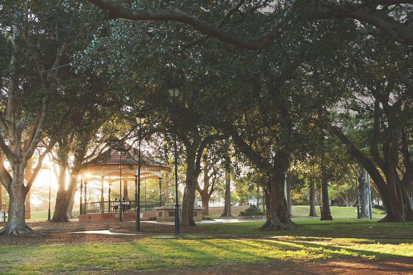 Park scene with trees and a gazebo in sunlight