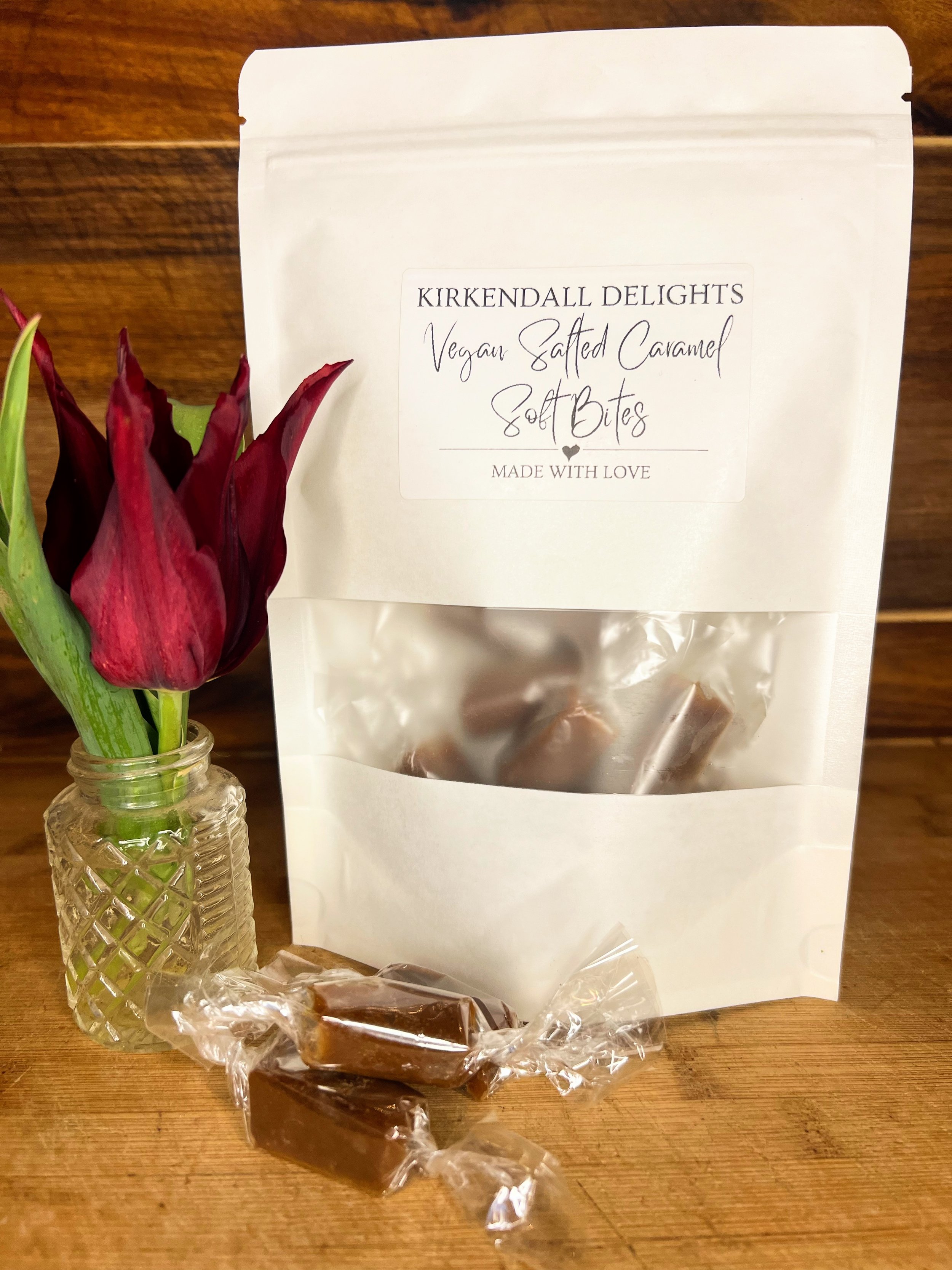 Bag of Kirkendall Delights vegan salted caramel soft bites with wrapped caramels and a red tulip in a glass vase, handmade with love