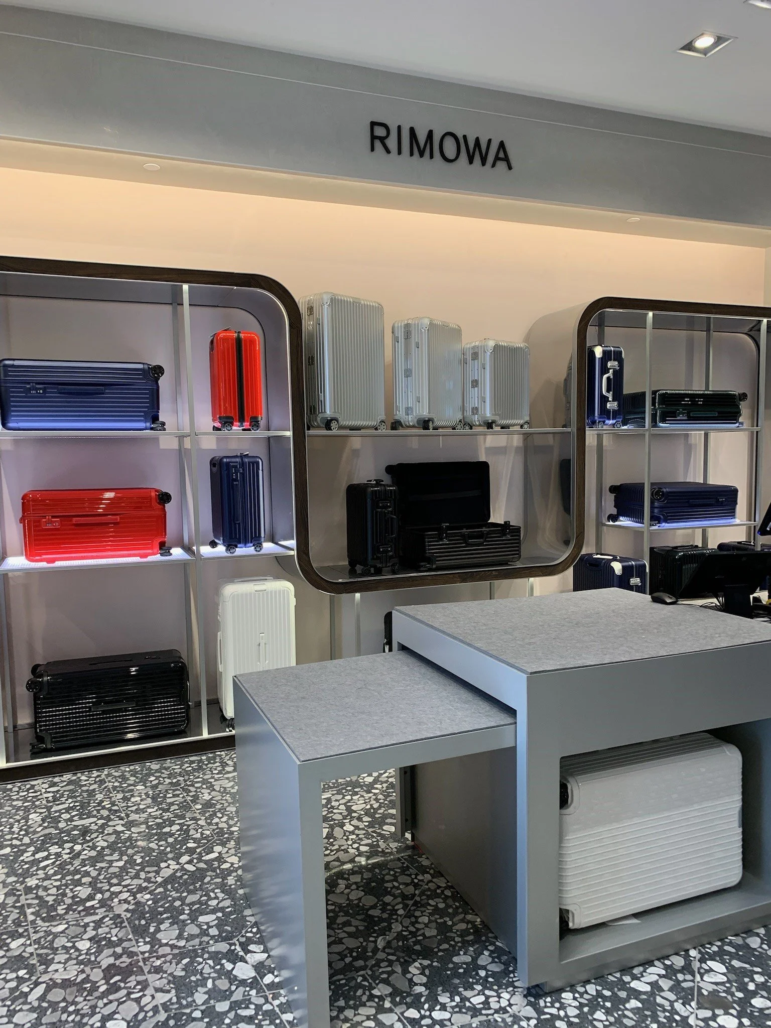 Display of various colorful suitcases and travel bags at a Rimowa store.