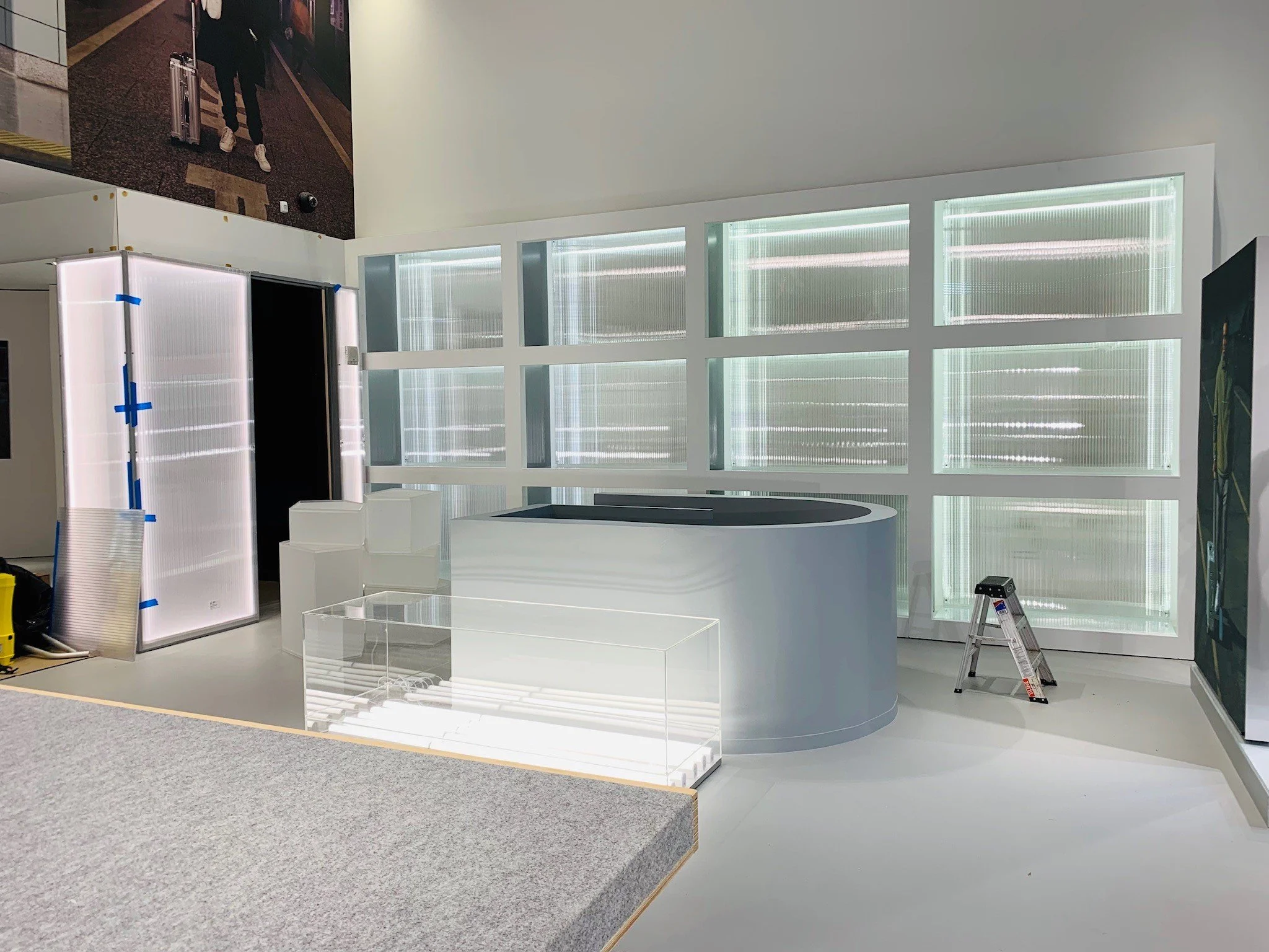 Empty modern interior space with white walls, a large curved counter, a small ladder, glass display case, and photo on the wall.
