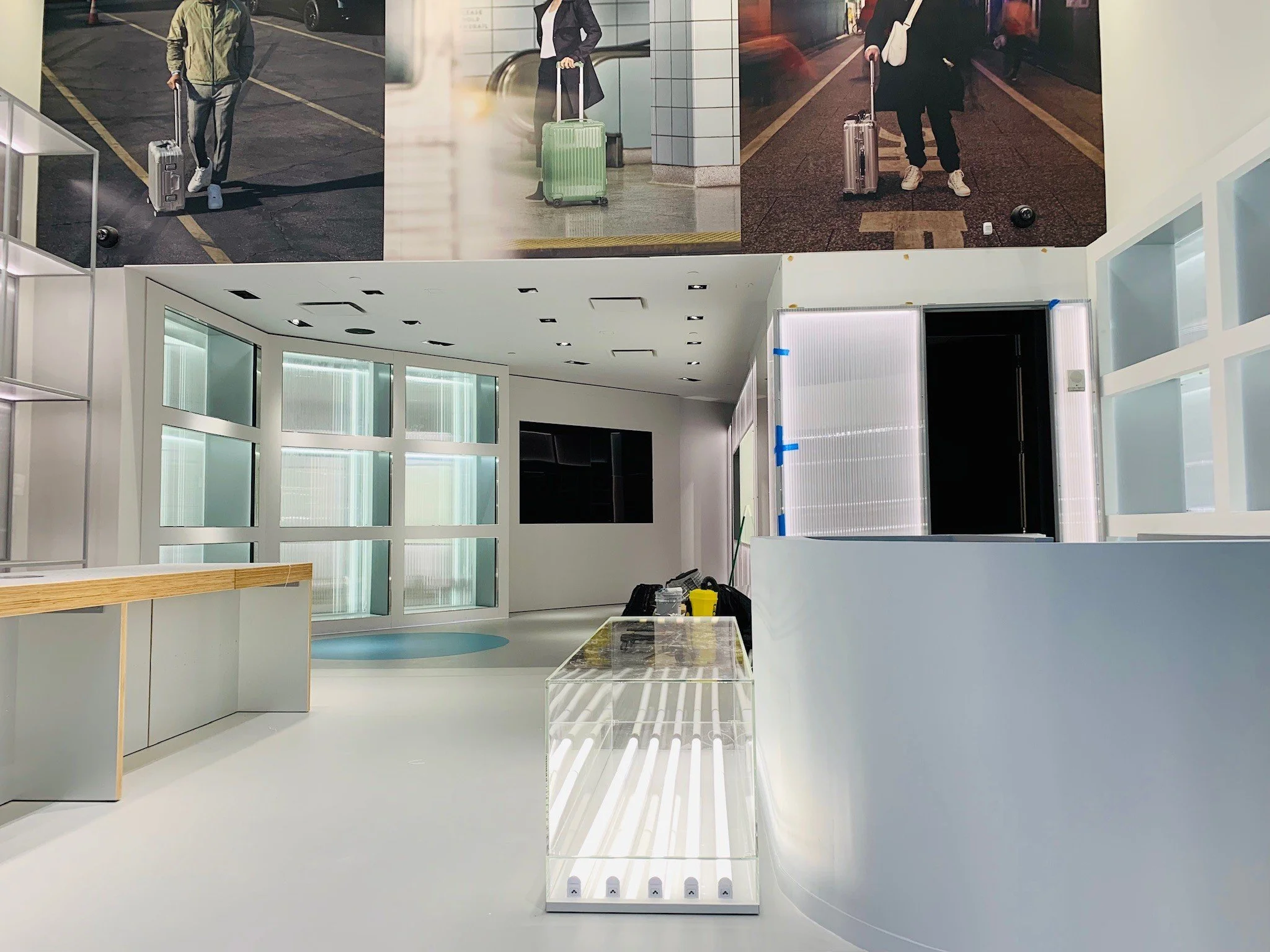 Empty modern interior space with large windows, white walls, and minimalistic furniture, including a glass display case and a wooden countertop.