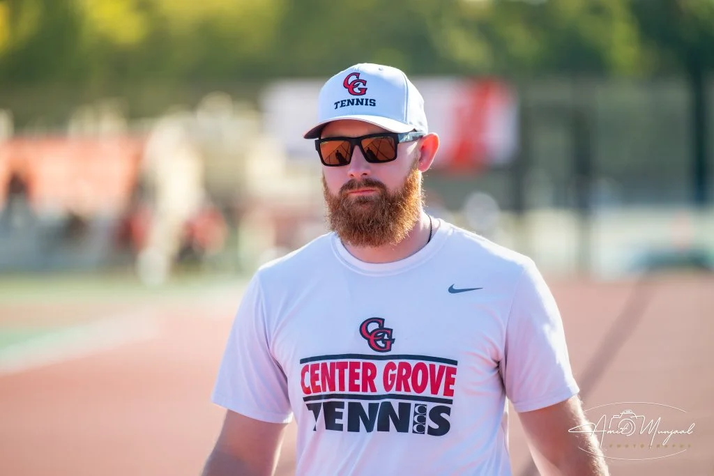 Smiling woman with glasses, hoop earrings, layered necklaces, and curly afro hairstyle.