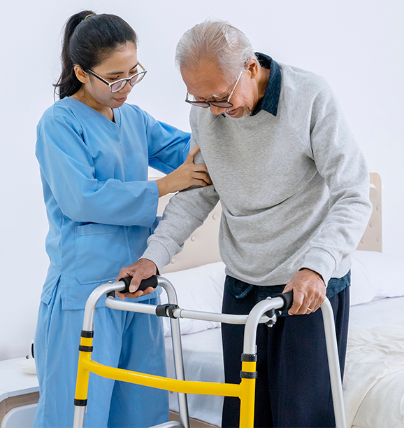 A nurse helping an elderly man walk with a walker in a healthcare facility.