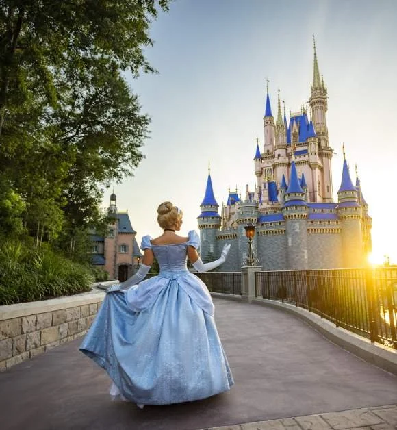 A woman dressed as Cinderella walking towards a castle at Disneyland during sunset.