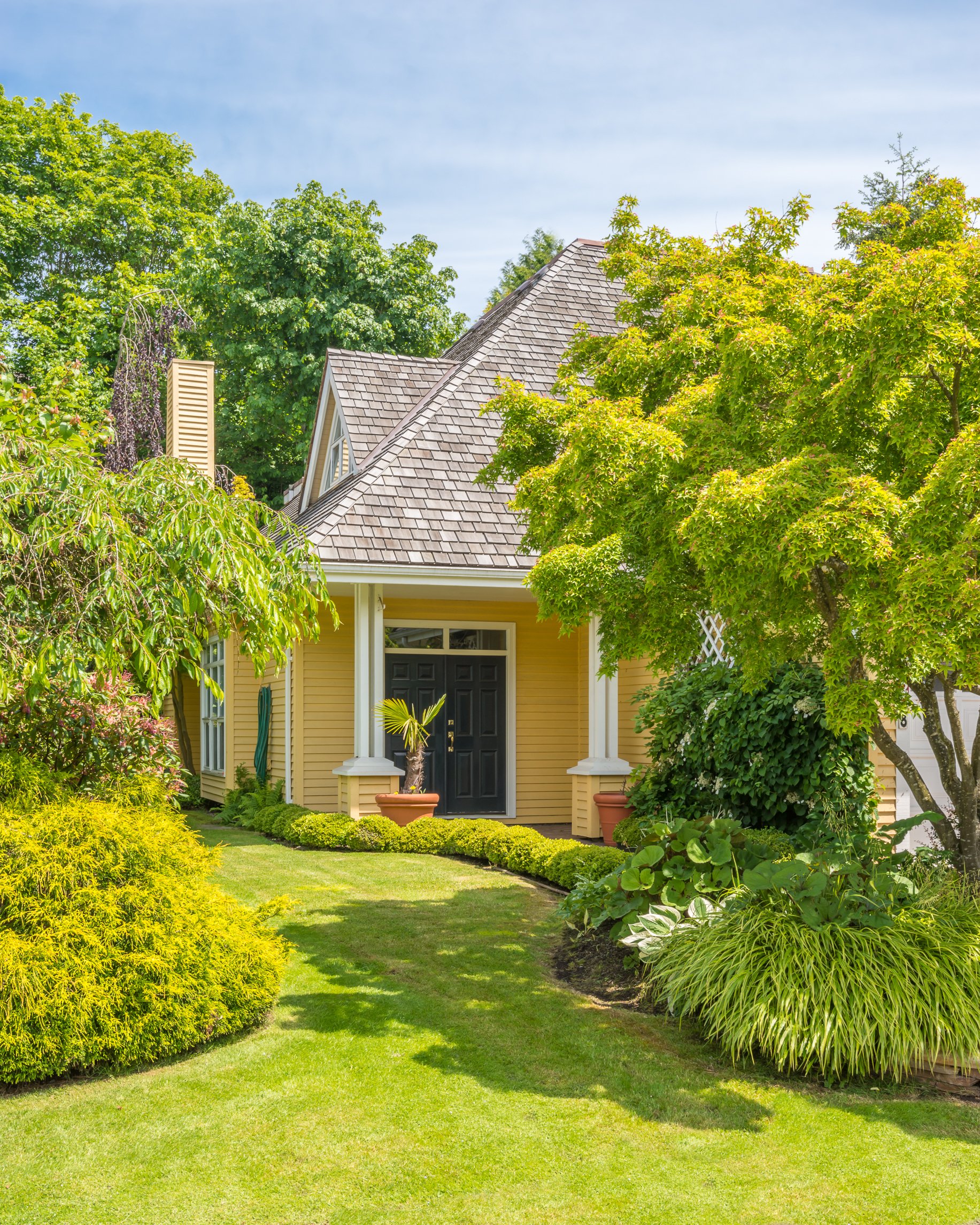 A front yard with a yellow house, green trees, and a well-maintained lawn.