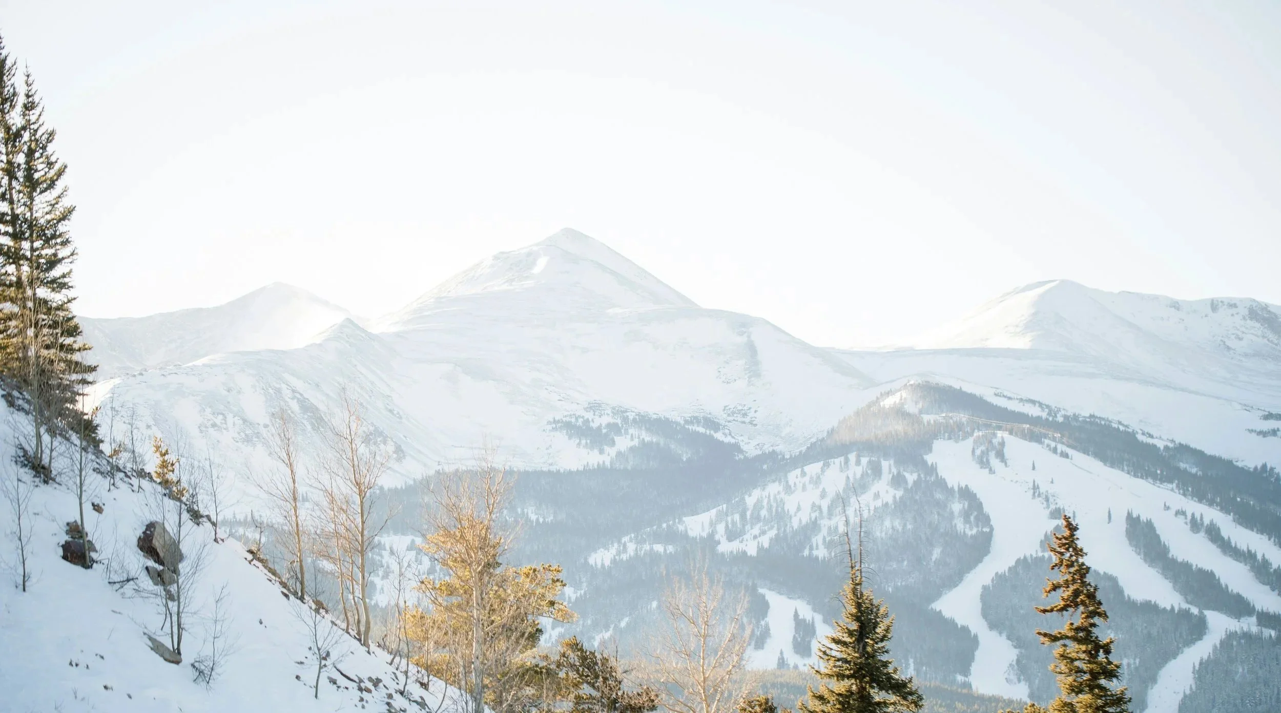 Snow-covered mountain range in Summit County, Colorado with ski runs and evergreen trees in the foreground.