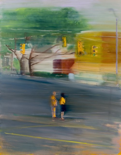 Two people in yellow shirts standing near a traffic light at an intersection with trees and colorful buildings in the background.