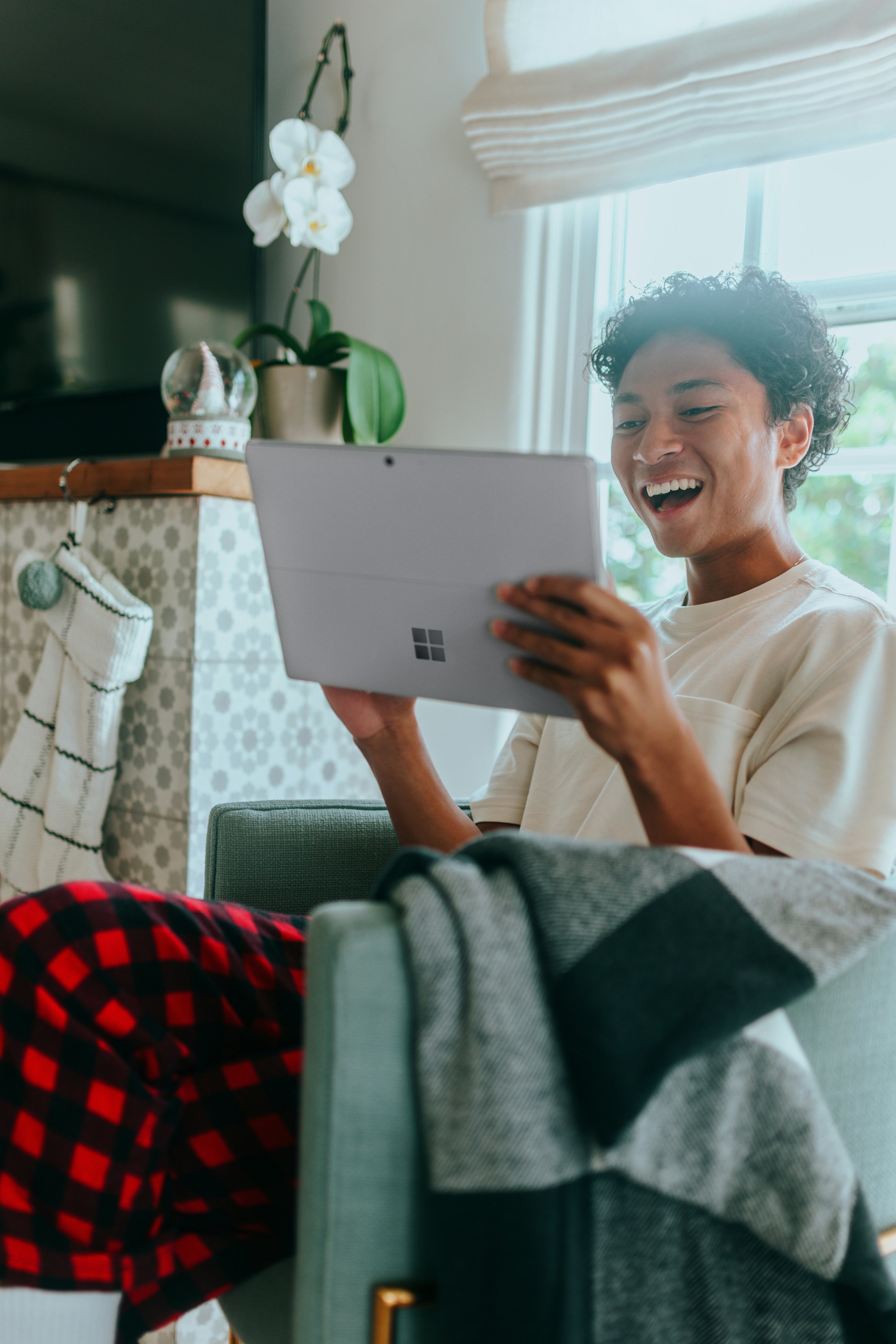 A young person of color sitting in a living room, smiling and looking at a tablet device they are using for their virtual therapy session.