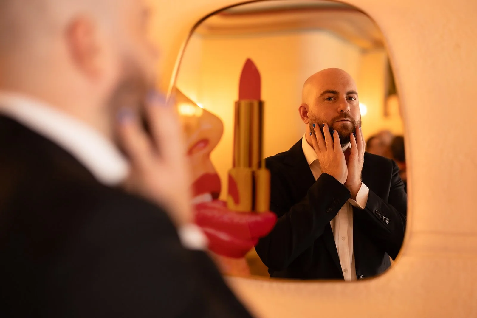 Man looking at himself in a mirror with lipstick shaped like a lipstick tube in the foreground