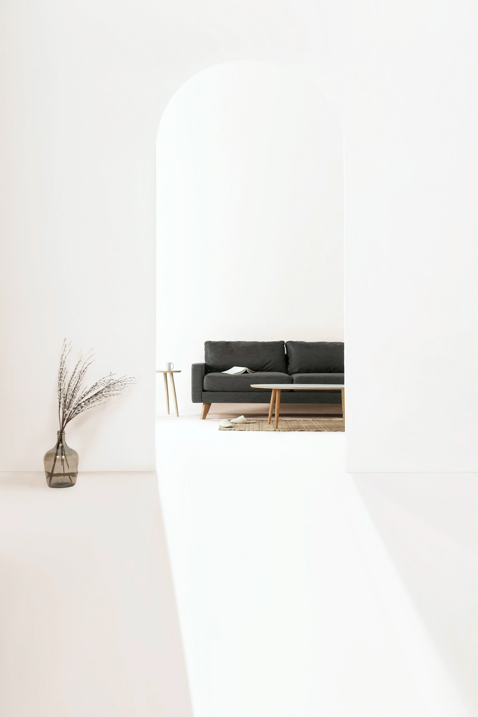 Minimalist living room with archway, dark gray sofa, coffee table, side table with a cup, open book, and decorative vase with dried branches.