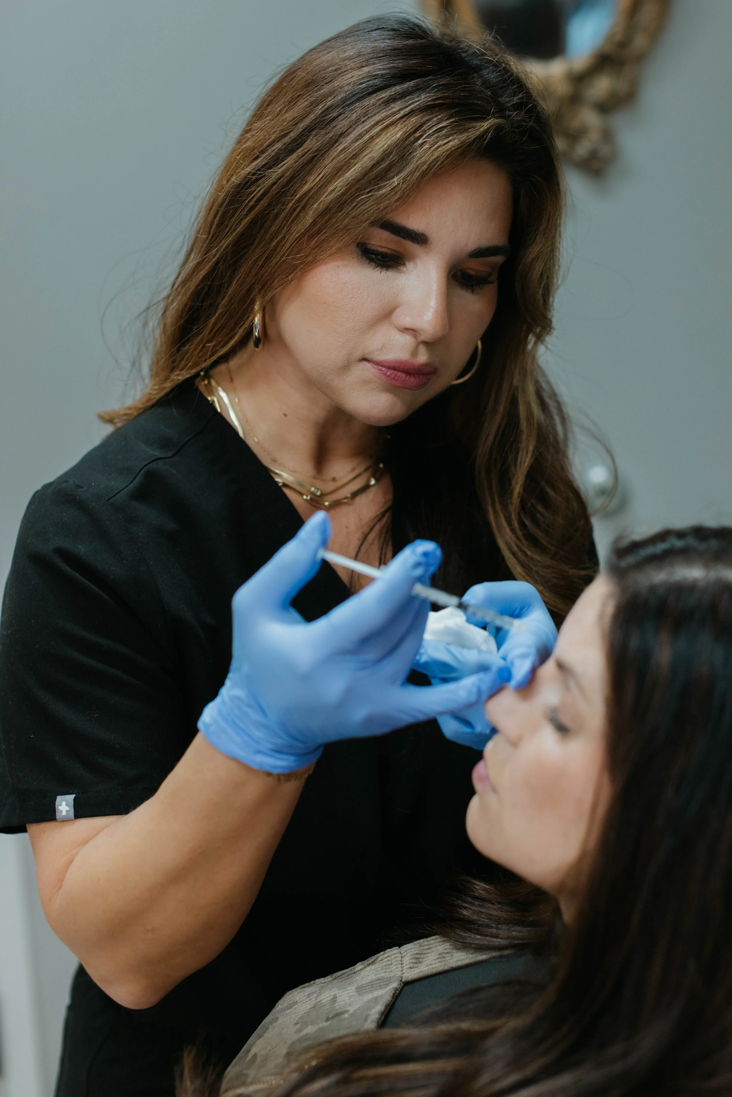 Woman in black uniform giving an injection to another woman's face.