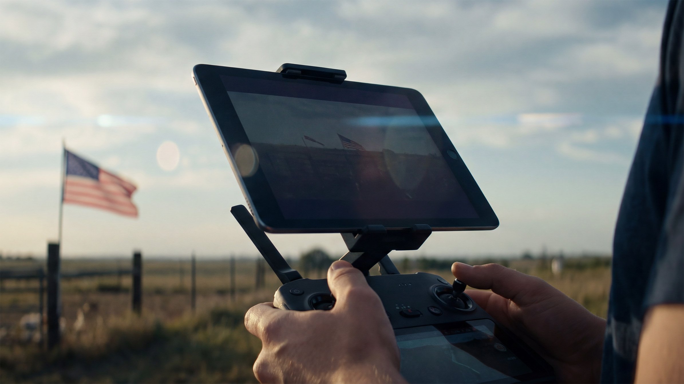 Close up of a drone pilot's hands holding a remote controller with a tablet showing flight data.