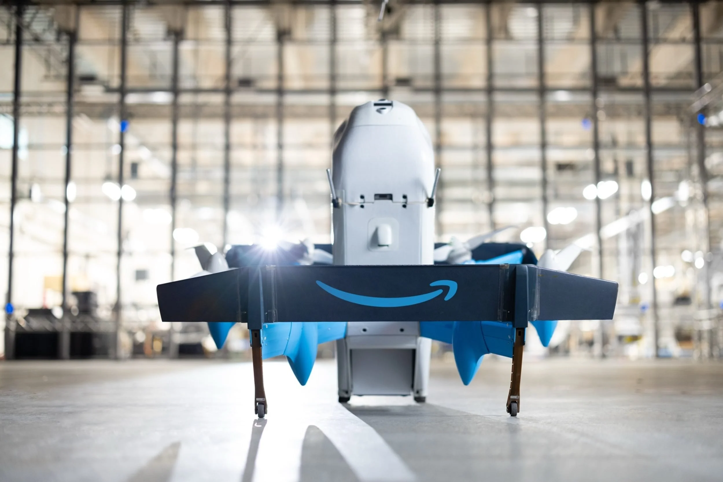Amazon MK30 delivery drone displayed in an indoor facility with Amazon branding and staff working nearby.