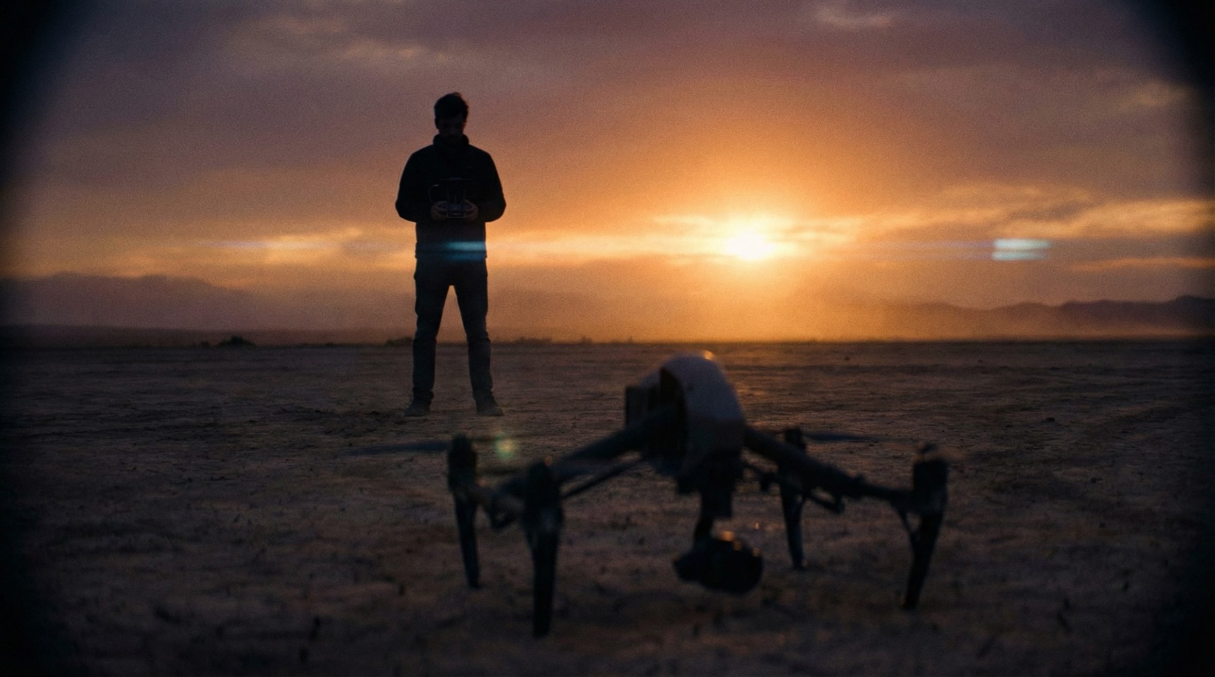 A drone on the ground at sunset with a pilot standing behind it.