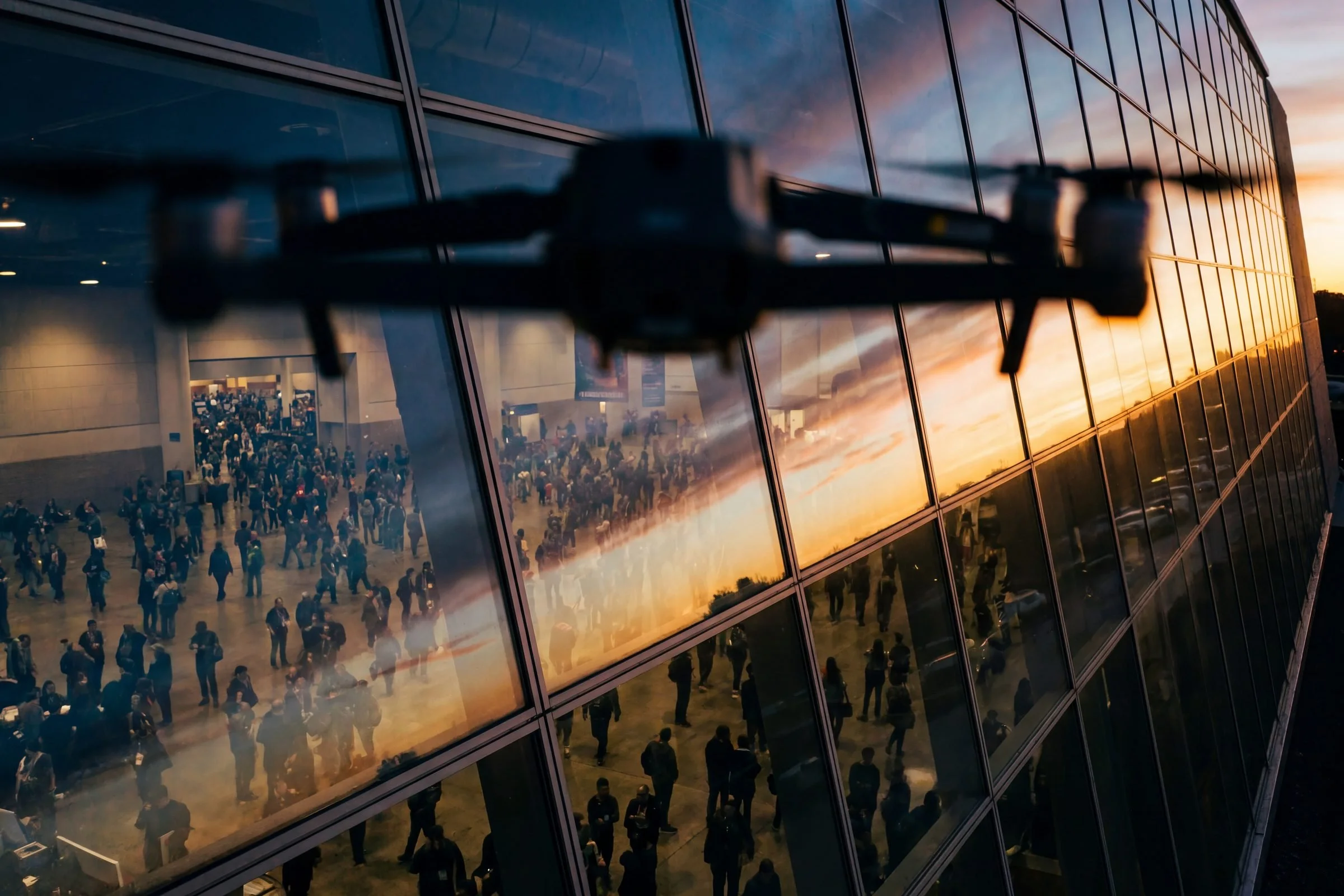 Drone flying outside a glass convention center during XPONENTIAL 2026 as crowds gather inside the venue