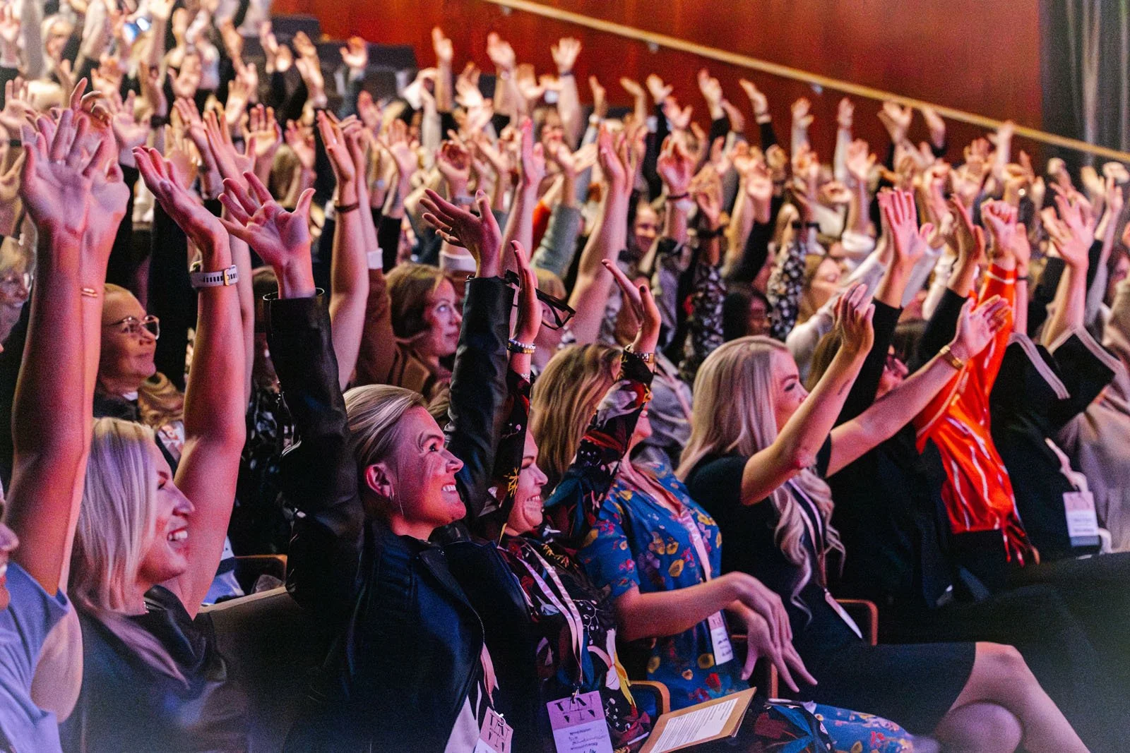 Kirjoittamaton tapahtuma, suuri yleisöä, kaikki istuvat ja osa seisoo, useita käsiä ylhäällä, iloisia ja hymyileviä ihmisiä.