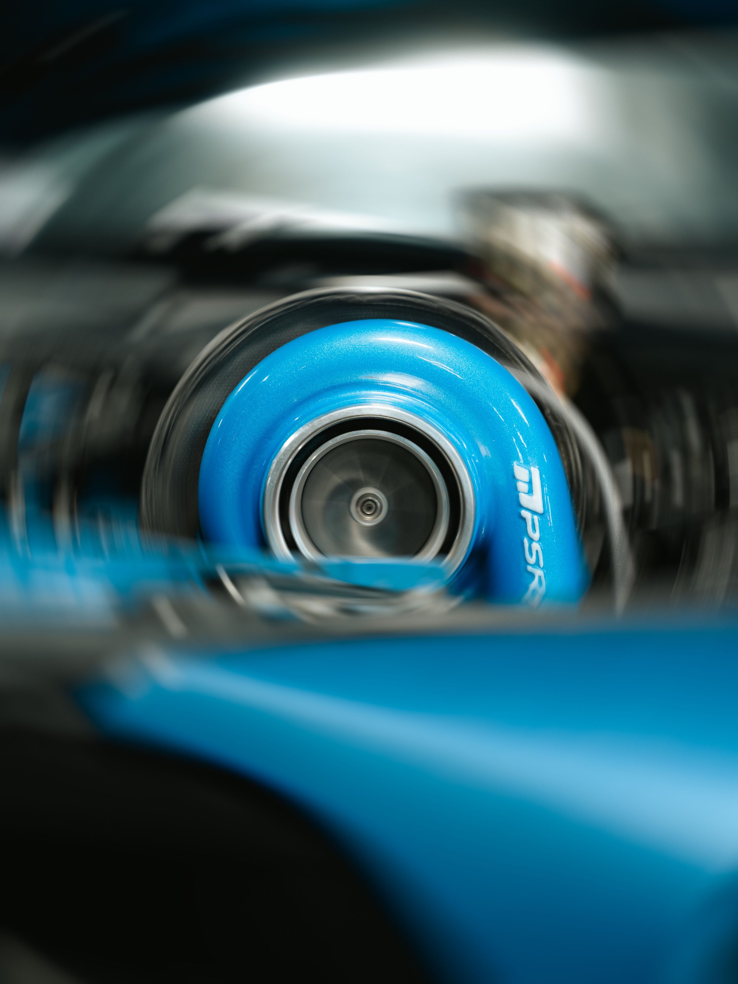 A close-up of a blue skateboard wheel in motion, with a blurred background.