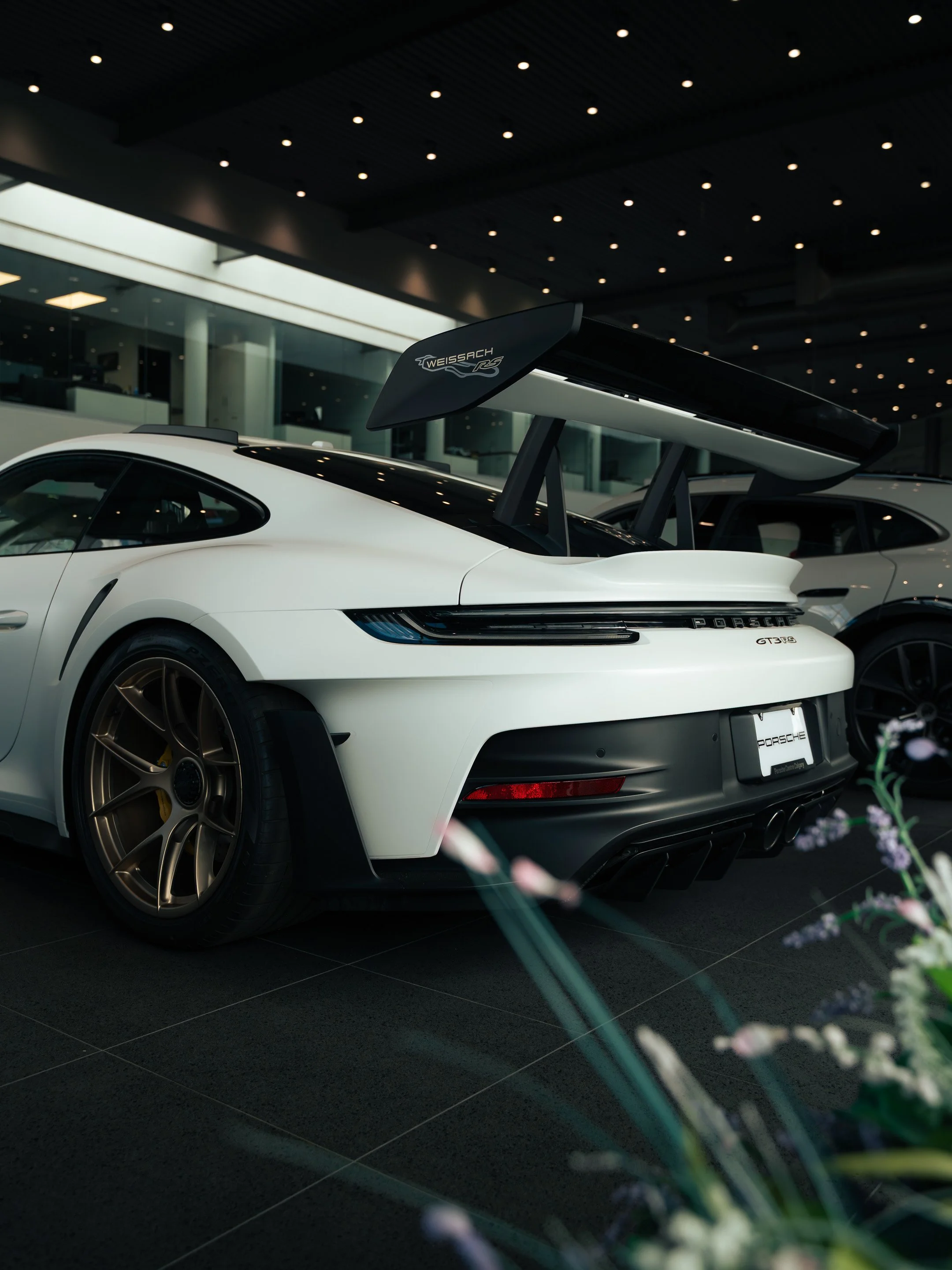 A white Porsche GT3 RS sports car with a large black rear wing inside a modern car showroom.
