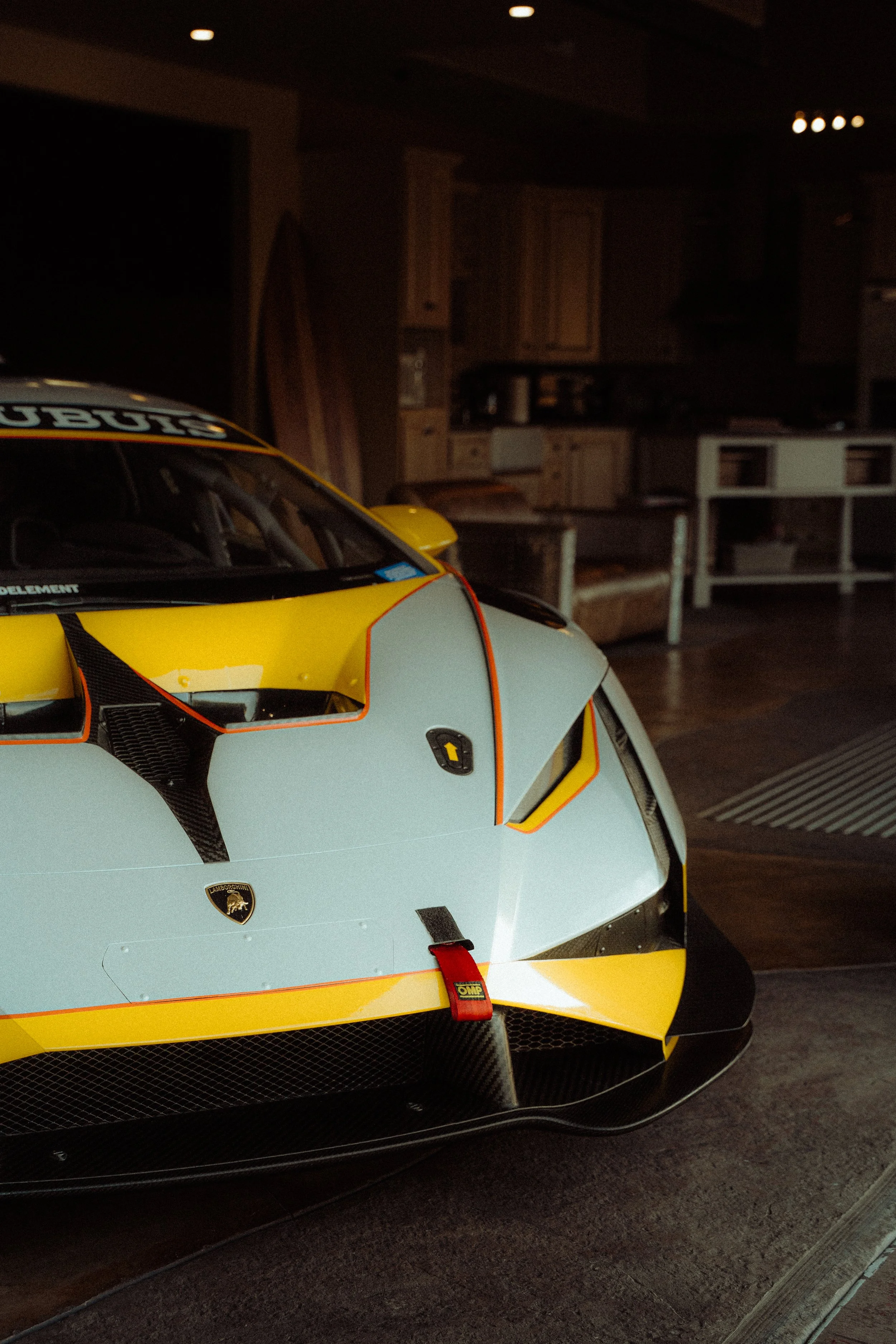 Close-up of a Lamborghini race car with yellow, black, and gray colors inside a dimly lit room.