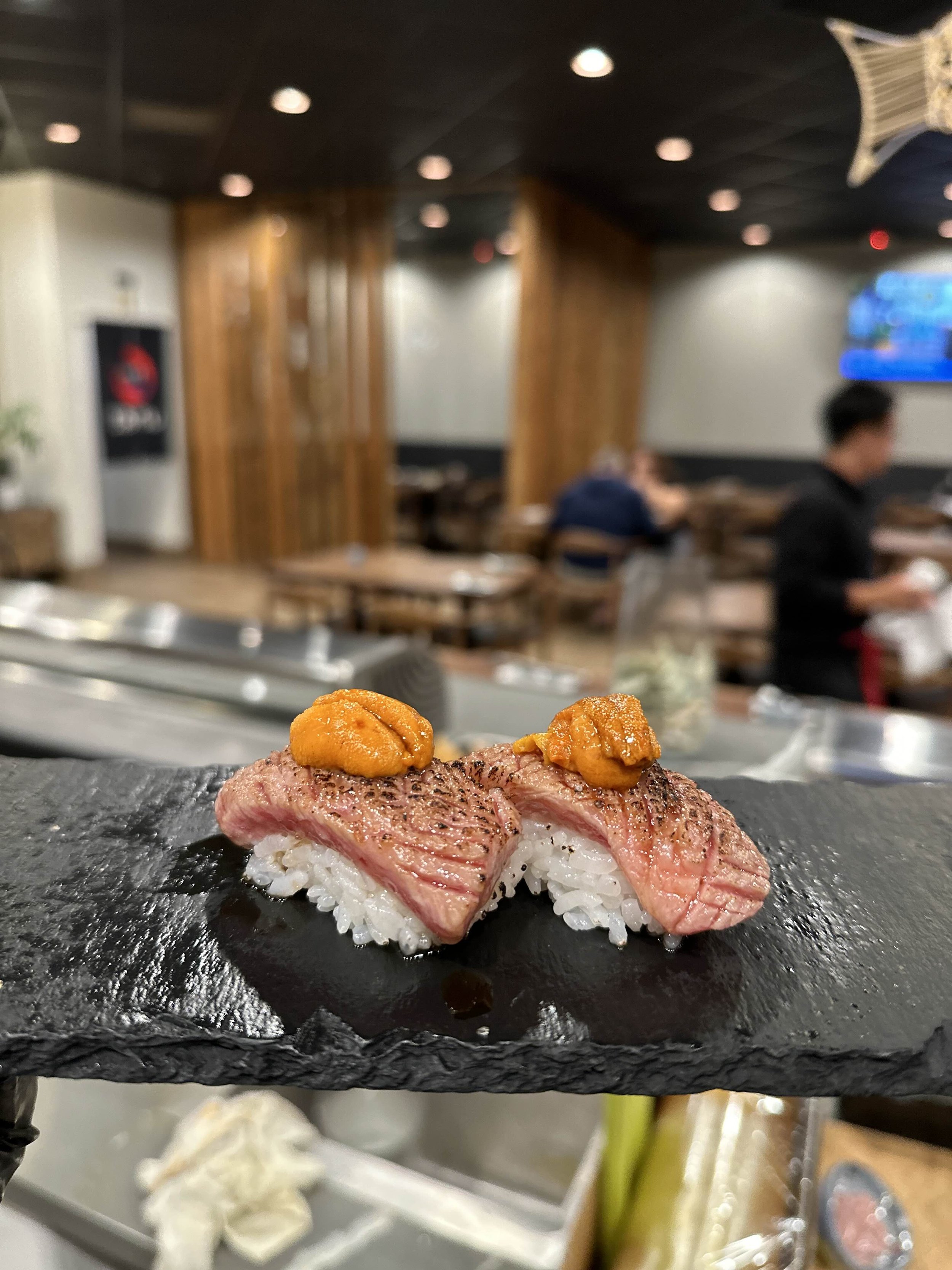 Seared sushi topped with uni on a slate platter in a restaurant setting.