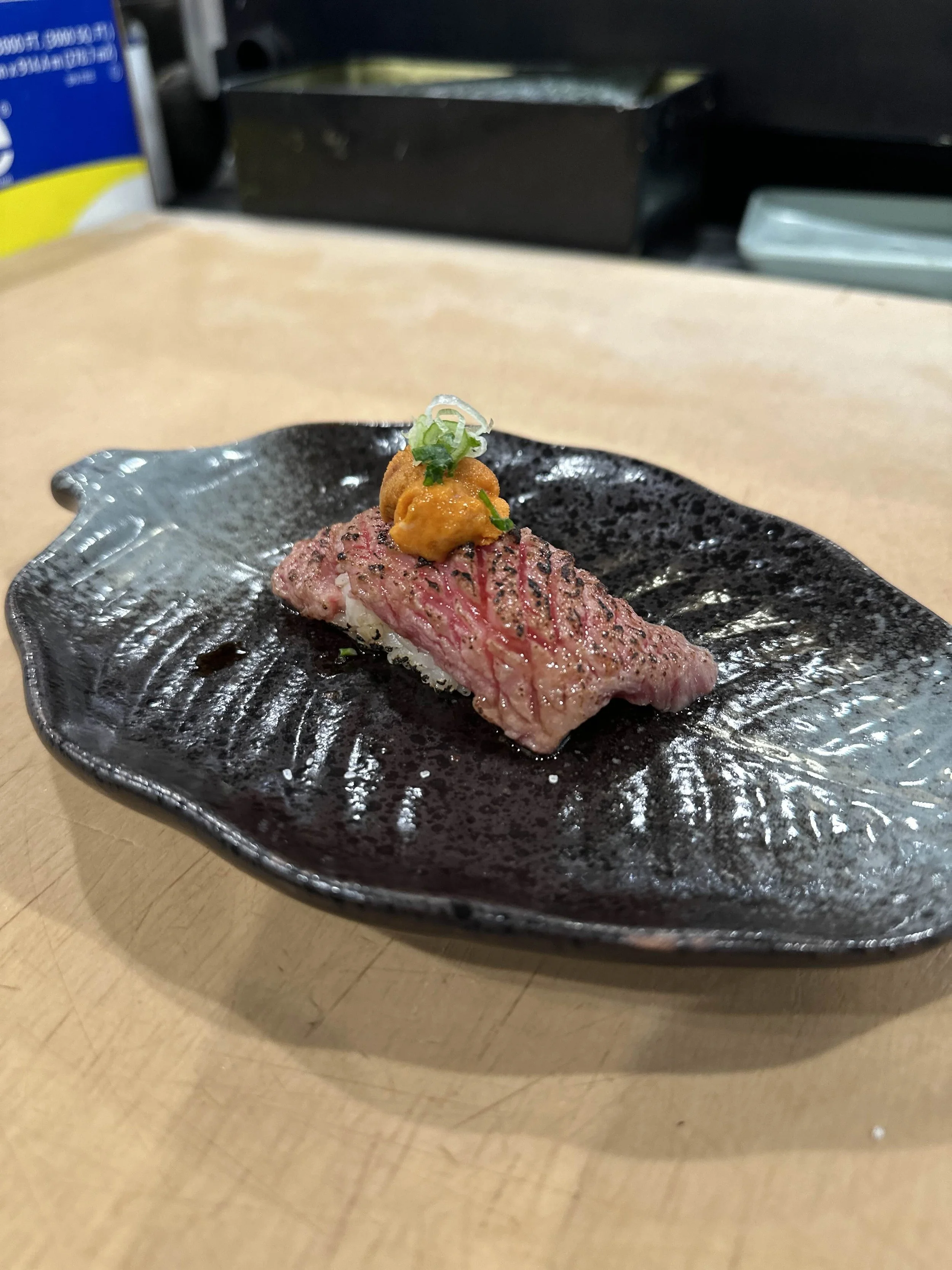 Sushi piece with seared beef and uni on black ceramic plate.