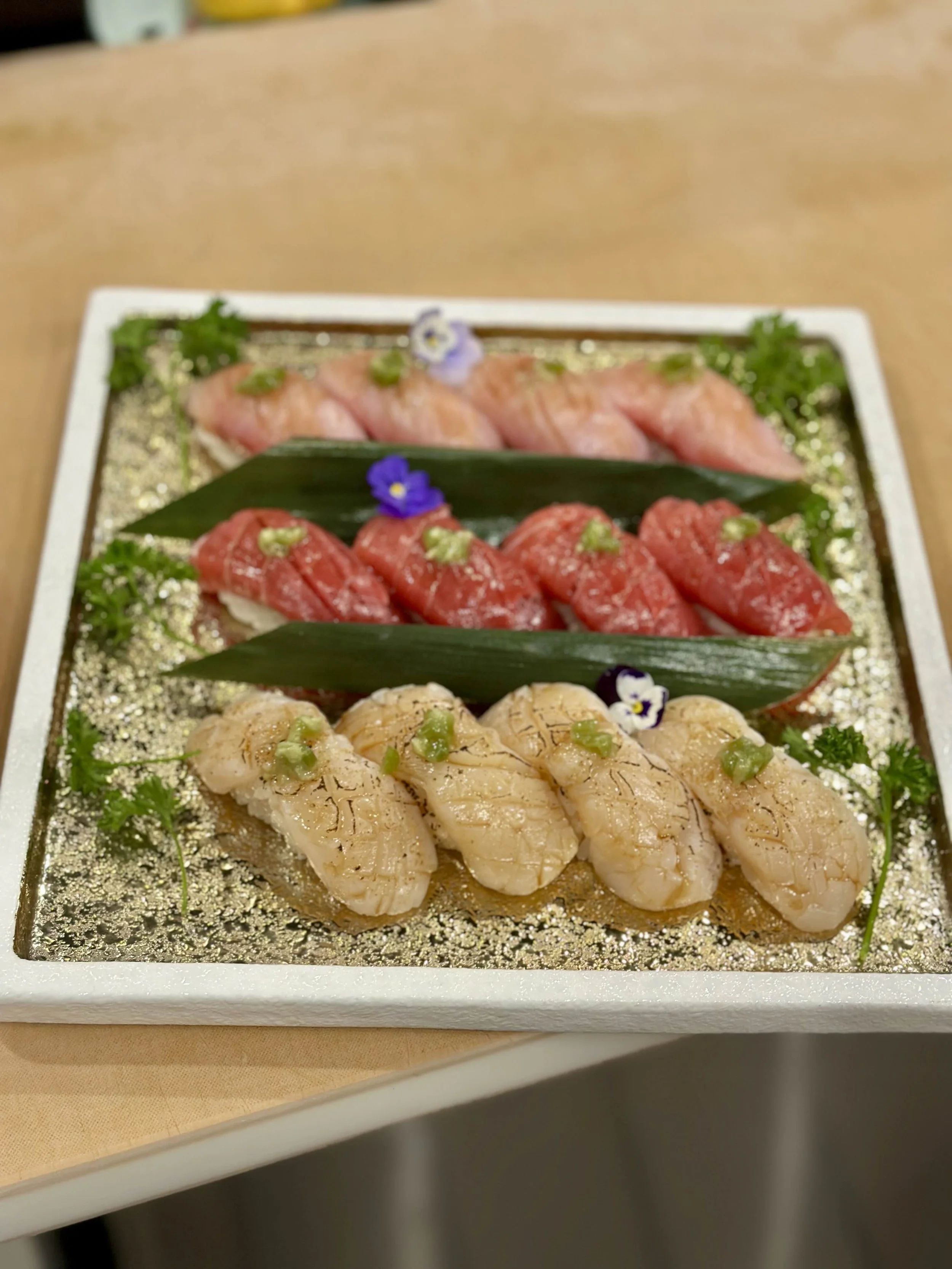 Assorted sushi nigiri on a decorative platter with garnish and edible flowers.
