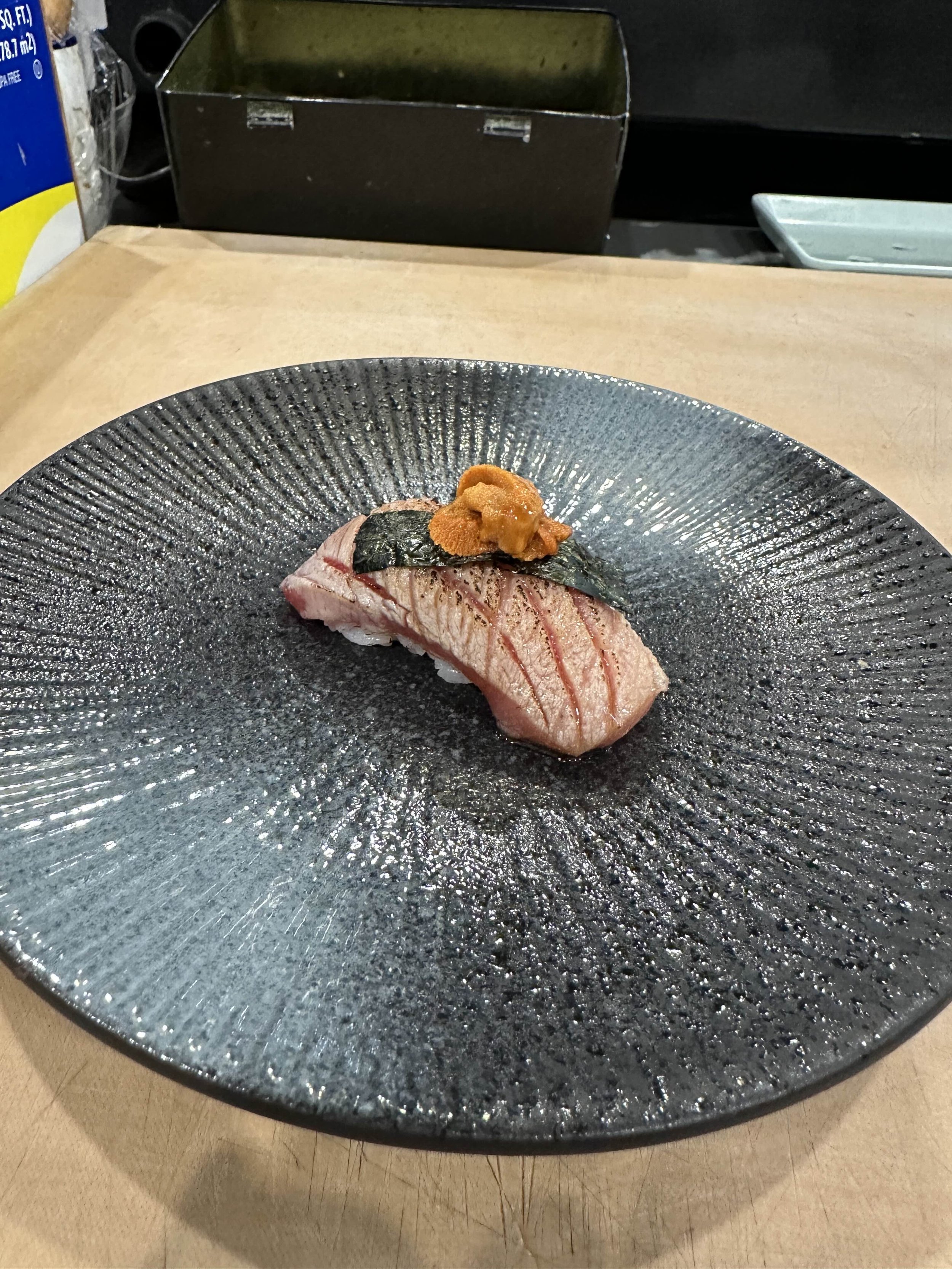 Sushi on a textured black plate, topped with sea urchin (uni) and seaweed.