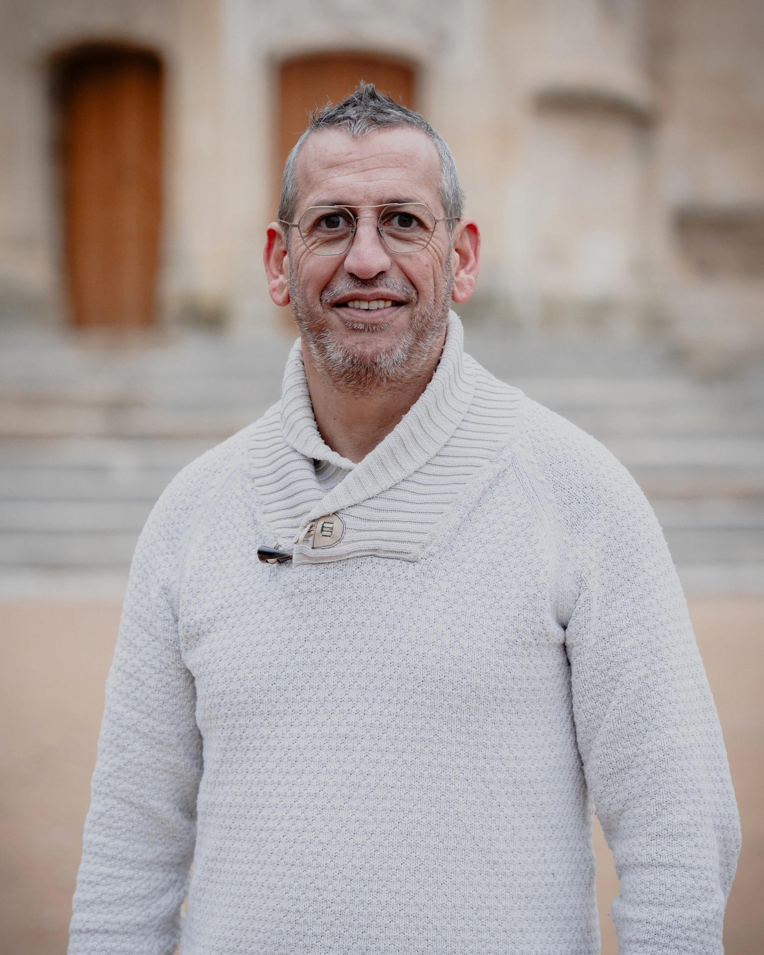 Homme souriant portant un pull blanc avec un fond architectural