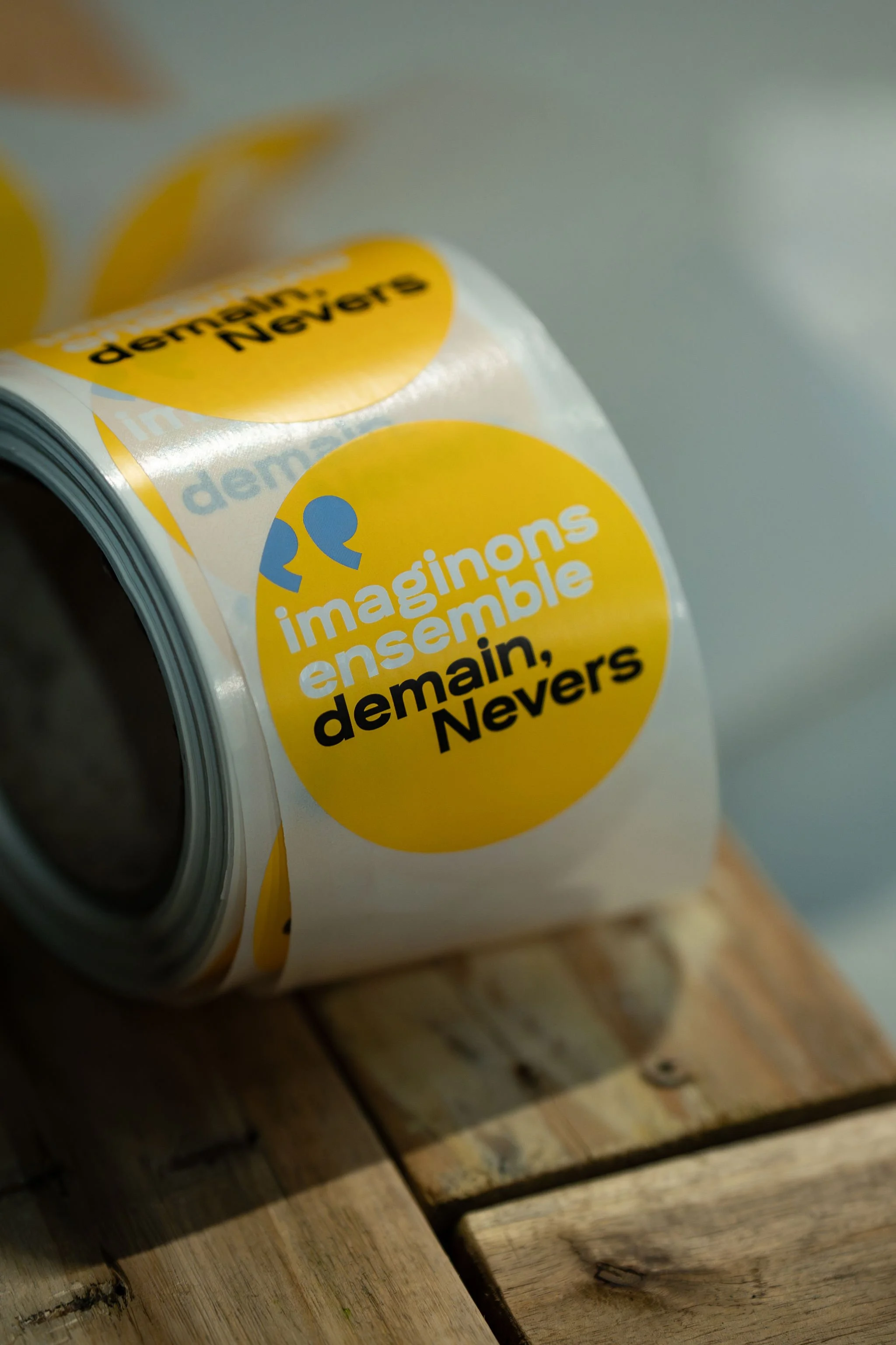 Rouleau de ruban adhésif avec une citation en français : "imaginons ensemble demain, Nevers", posé sur un plan en bois.