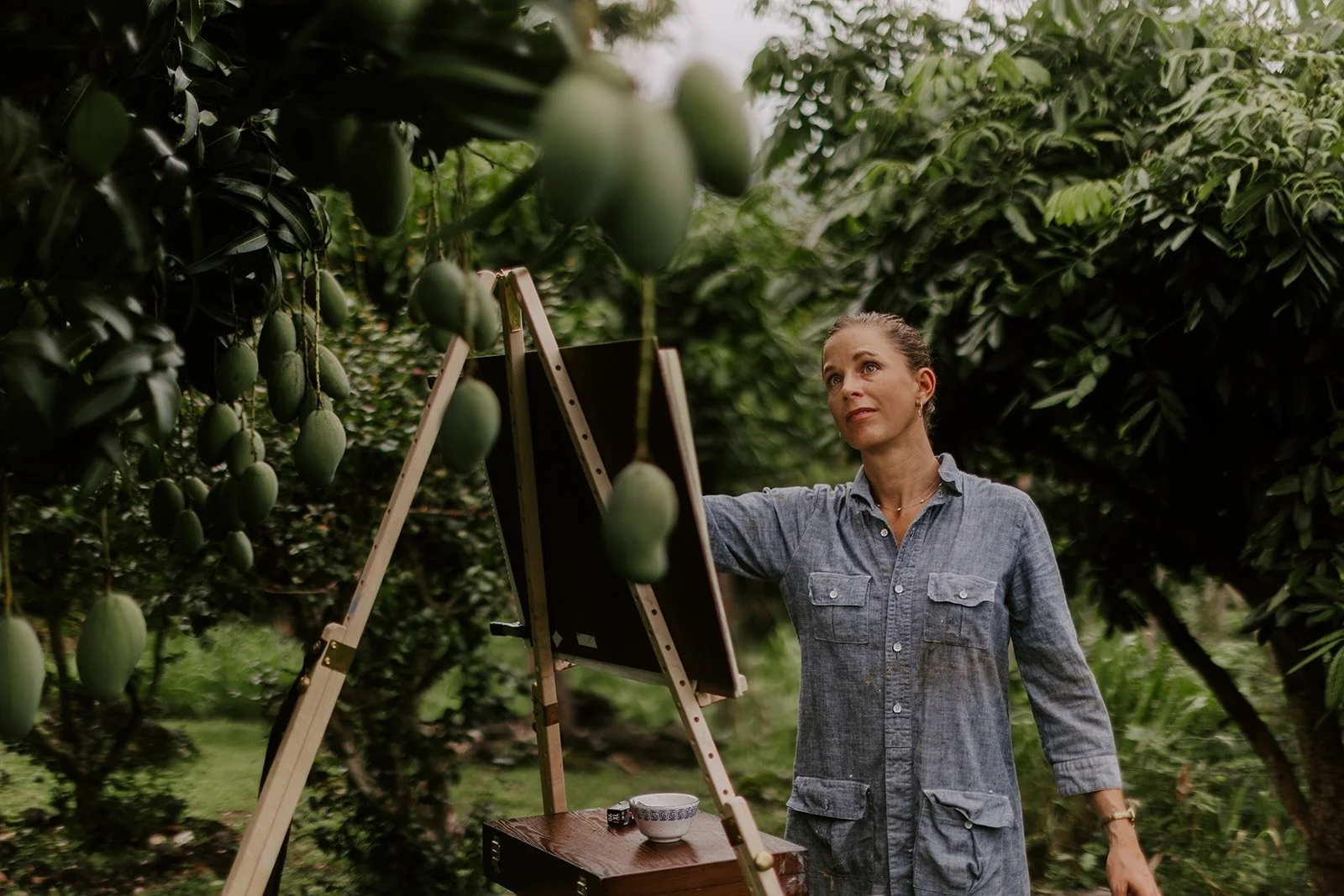 Hawaii based wedding artist painting in a mango orchard. Lush, green outdoor setting.