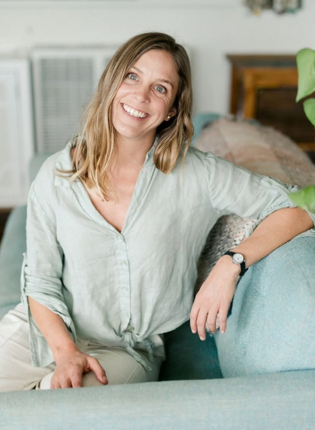 Artist Smiling sitting on an aqua blue couch with a sage green shirt