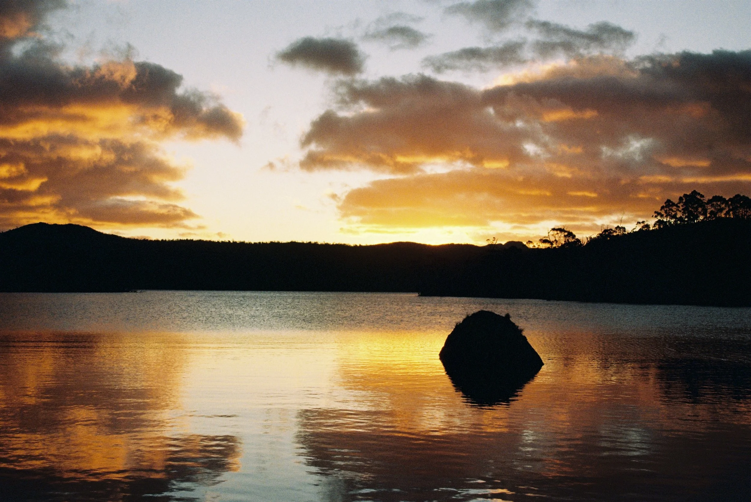 Alpine lake at sunset in Tasmania under high pressure, with calm water and small fair-weather cumulus humilis clouds.