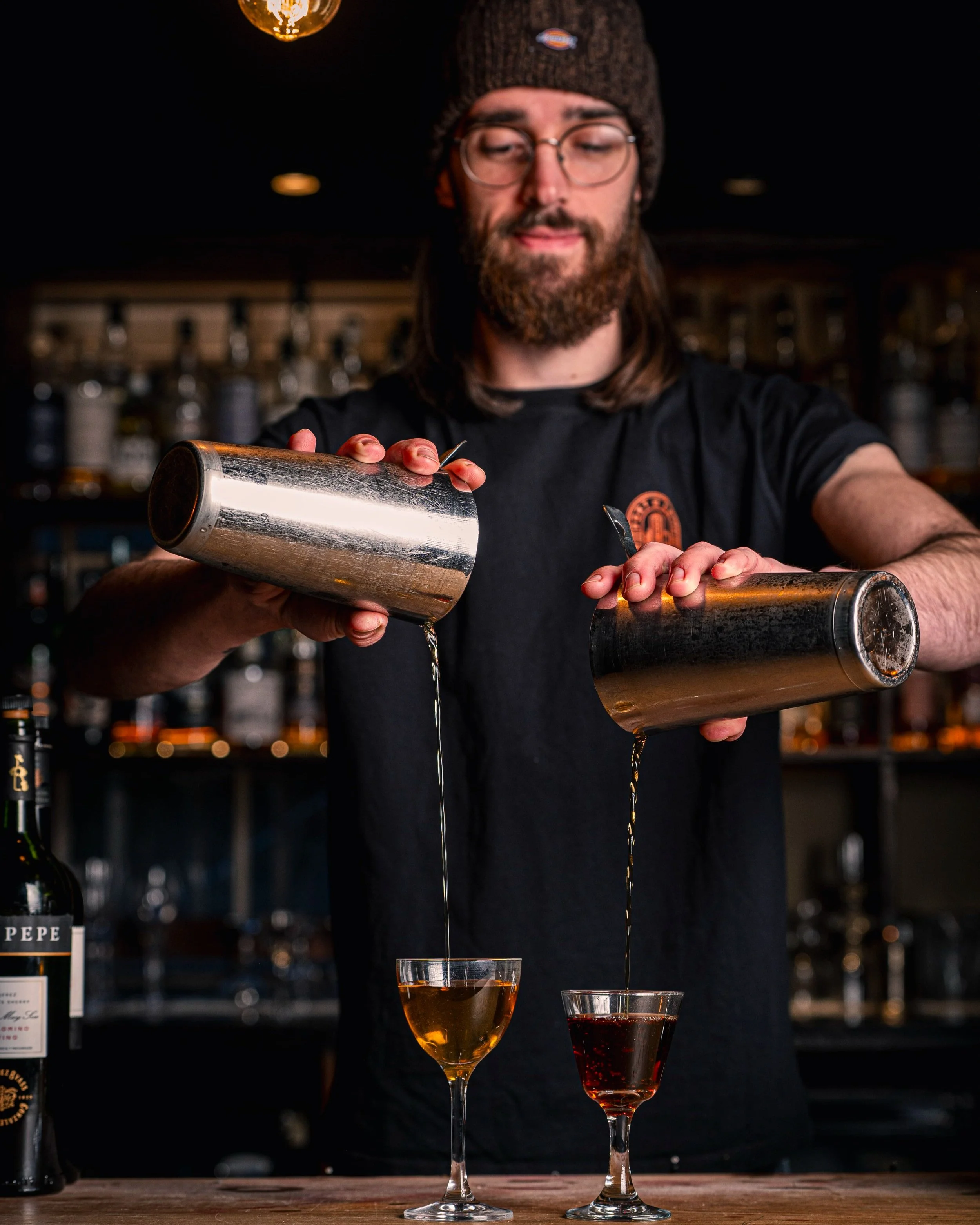 Bartender expertly pouring cocktails at Mothership bar.