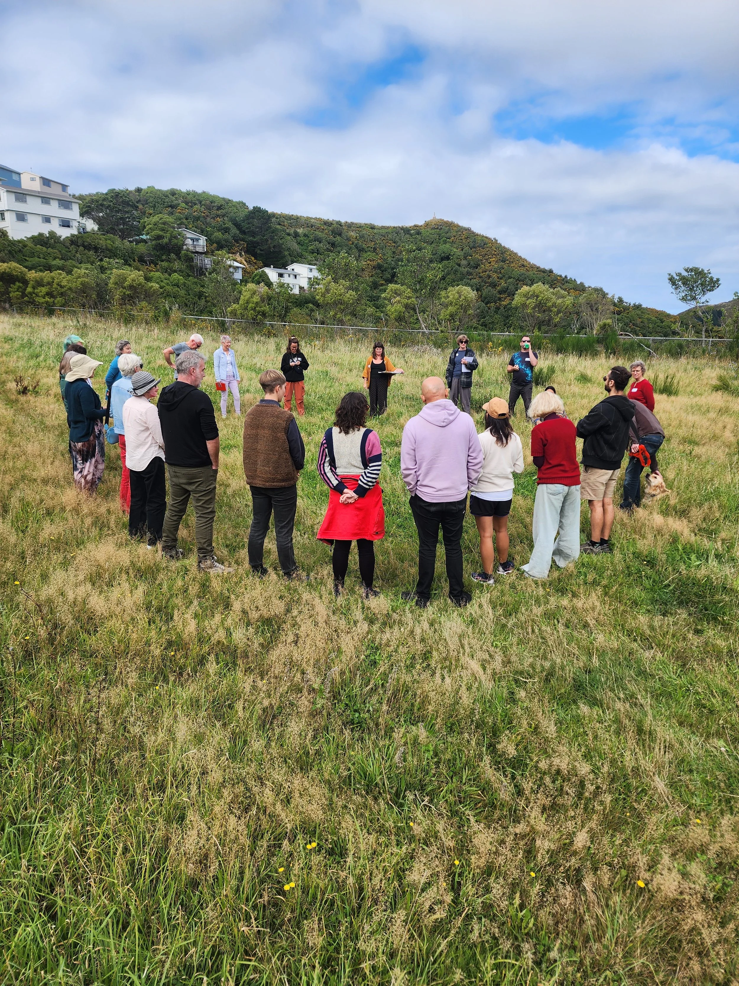 People gathered in a circle outdoors with hills behind