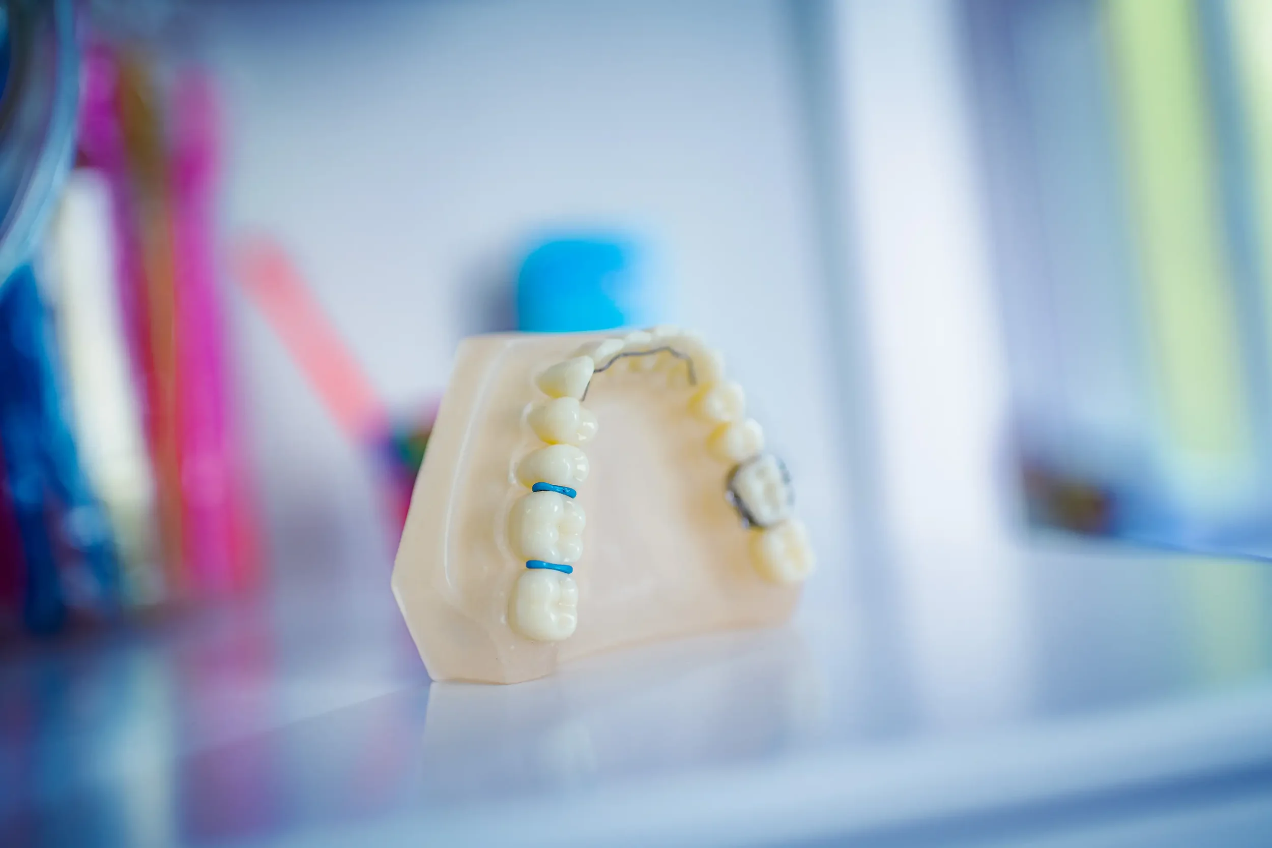 Zahnmodel mit Brackets auf einem blassen Unterkiefer, Standard-Schreibtisch, unscharfer bunter Hintergrund.