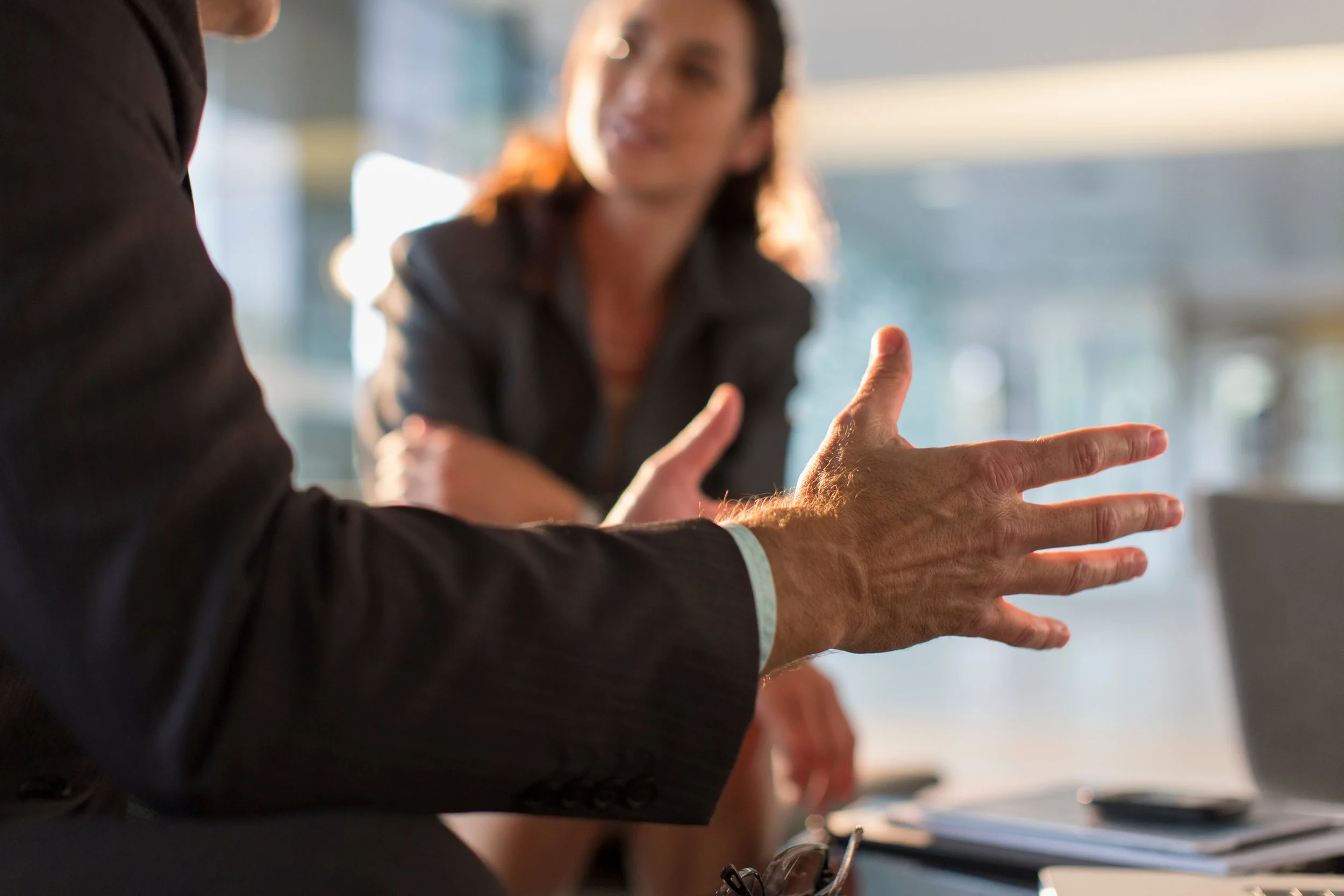 Two people engaged in a conversation at a business meeting, with one person gesturing with their hands and the other smiling.