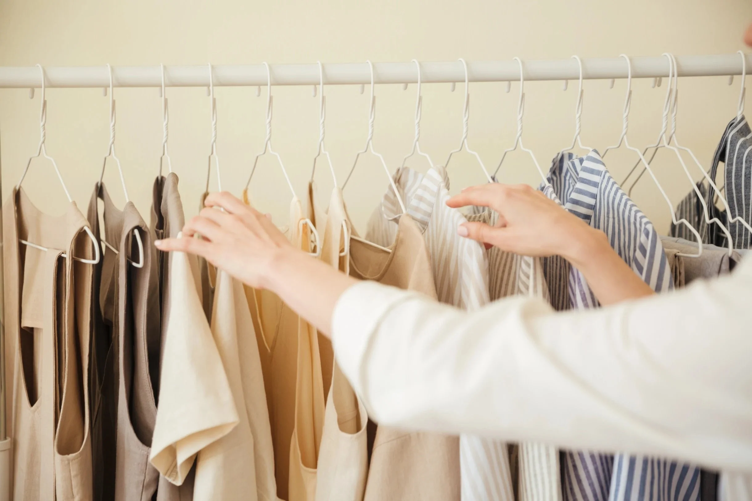 Hands organizing clothes on hangers in a neatly arranged closet.