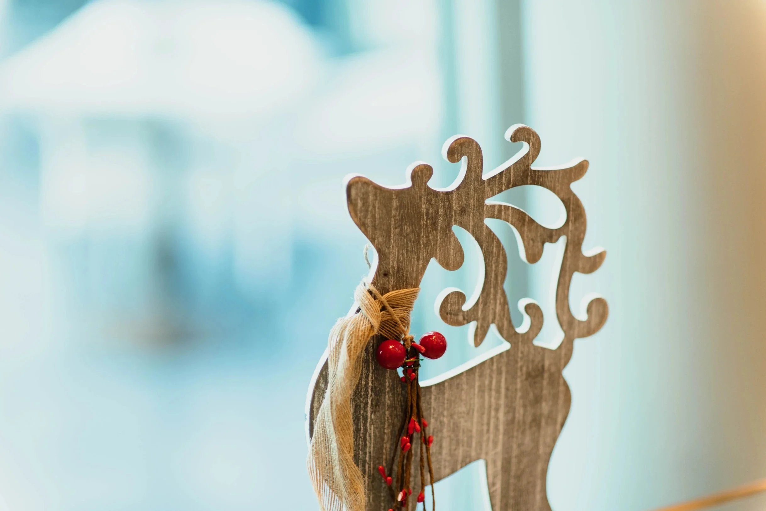 Wooden reindeer holiday decoration with red berry accents on a soft blurred background.