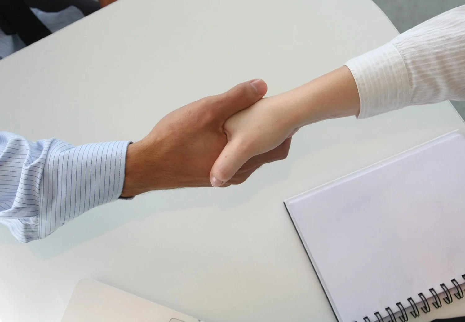 Two people shaking hands over a table, representing personalized concierge service and client support.