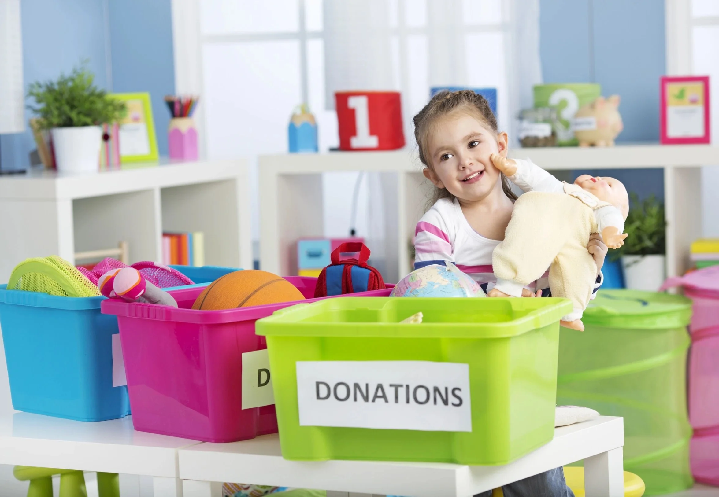 Child placing toys into labeled donation bins in a bright room.