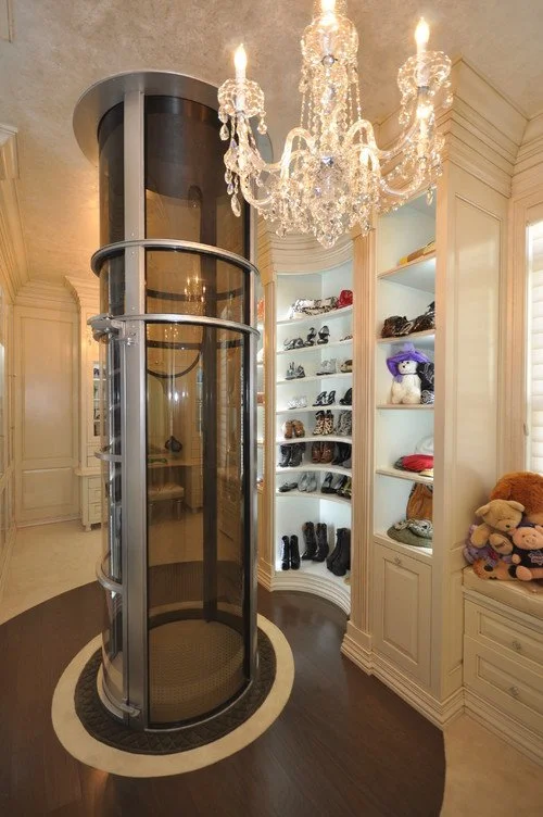 Luxury walk-in closet with chandelier lighting and circular elevator closet system for shoes and clothing.